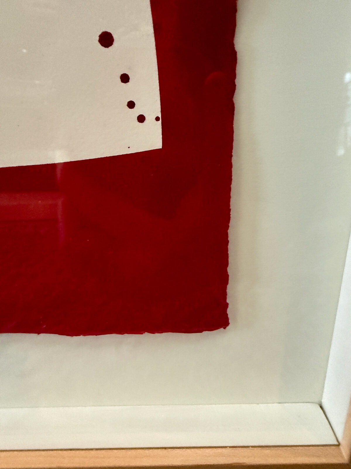 A framed abstract piece featuring bold red and black shapes against a white background with splattered ink.