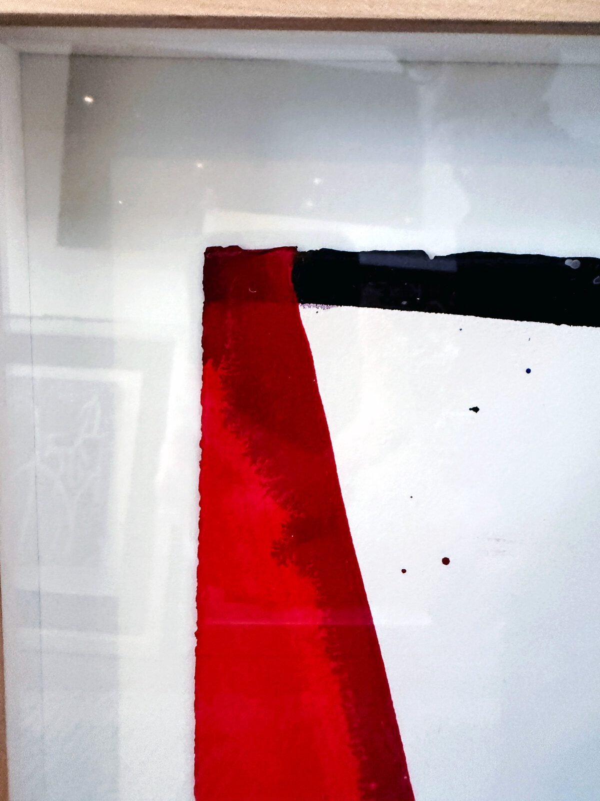 A framed abstract piece featuring bold red and black shapes against a white background with splattered ink.