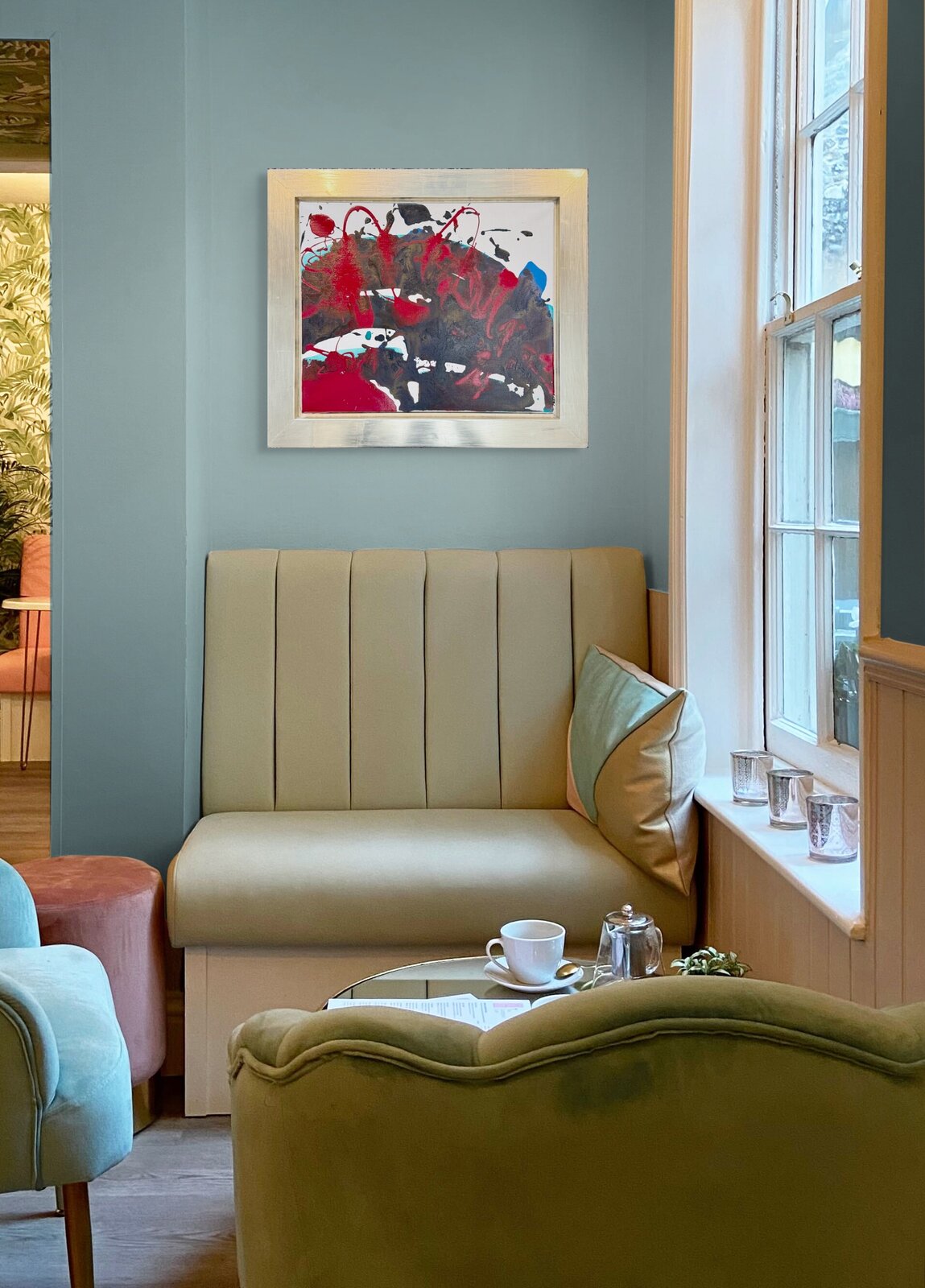 An abstract composition featuring bold red and black splatters against a white background, framed in metallic silver.