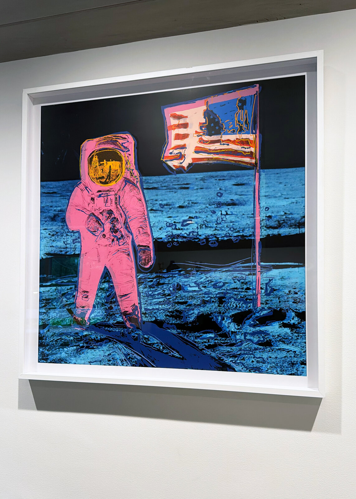 A pop-art style print of a figure in a spacesuit standing on a barren landscape next to a flag.