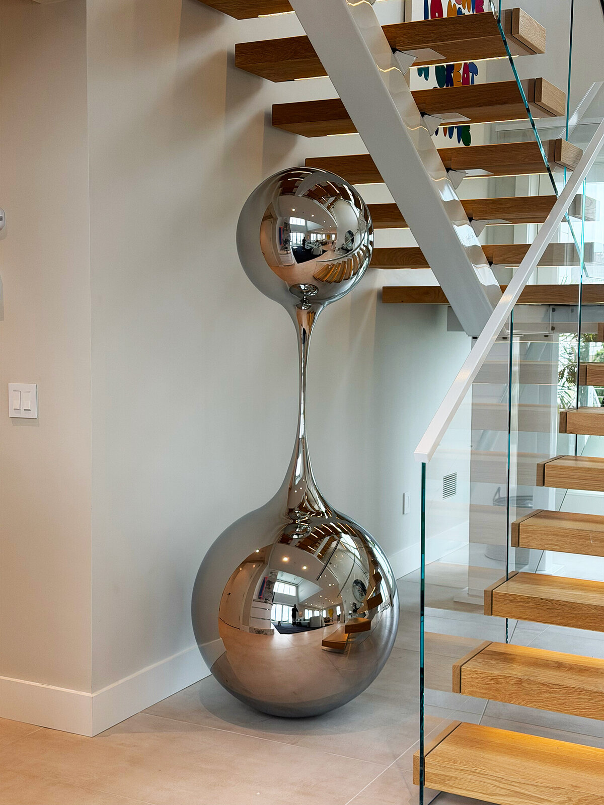 A reflective sculpture and a figure in green stand together in a modern glass atrium.