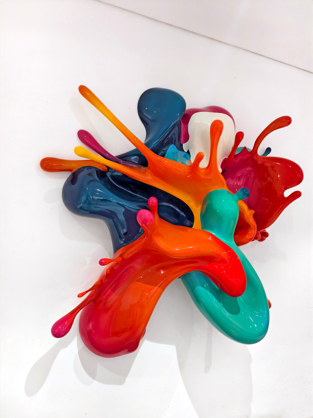 A dynamic sculpture of glossy, multi-colored paint splashes frozen in motion against a plain white background.