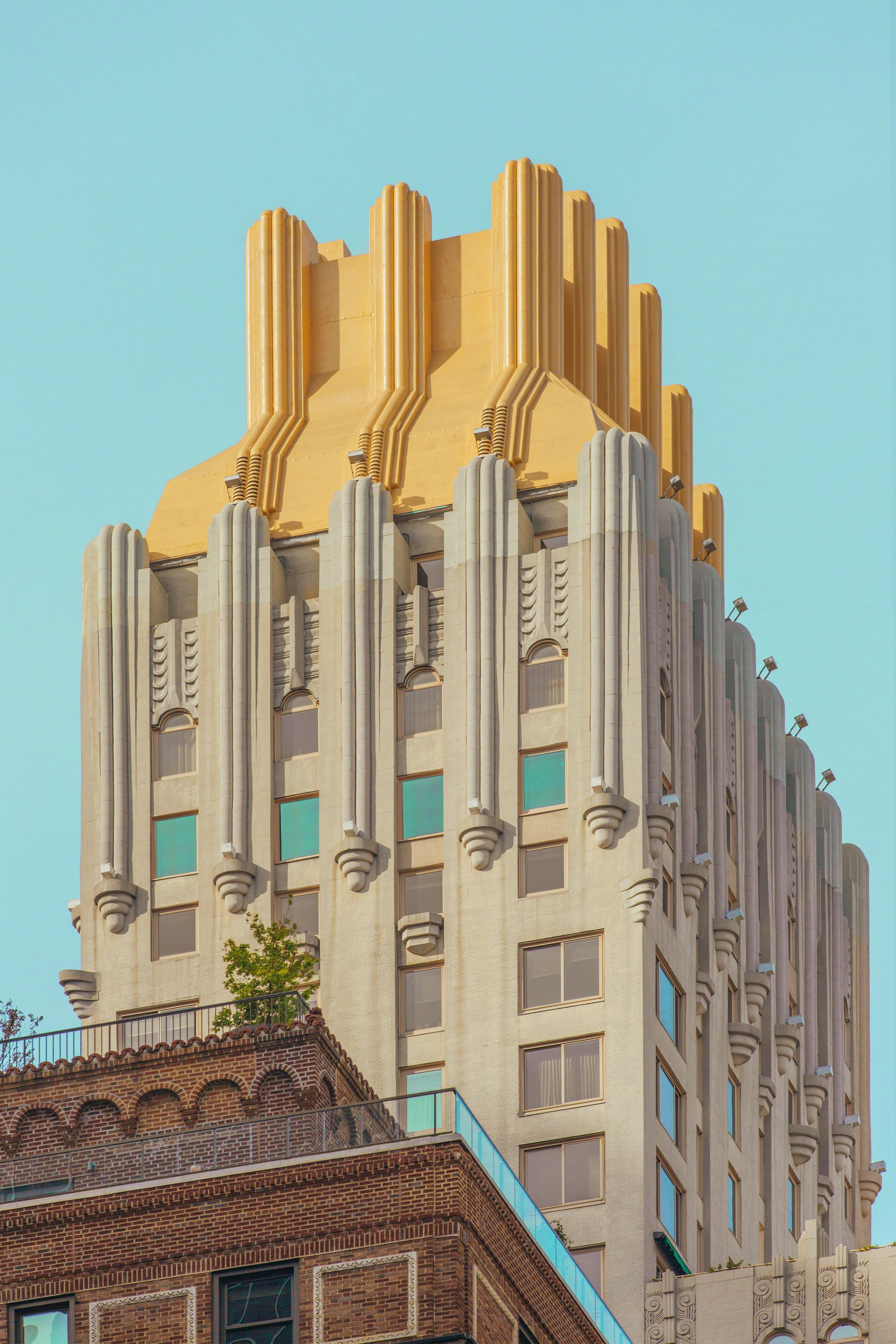 A vertical architectural composition featuring a beige building with a golden, Art Deco-style roof against a clear blue sky.