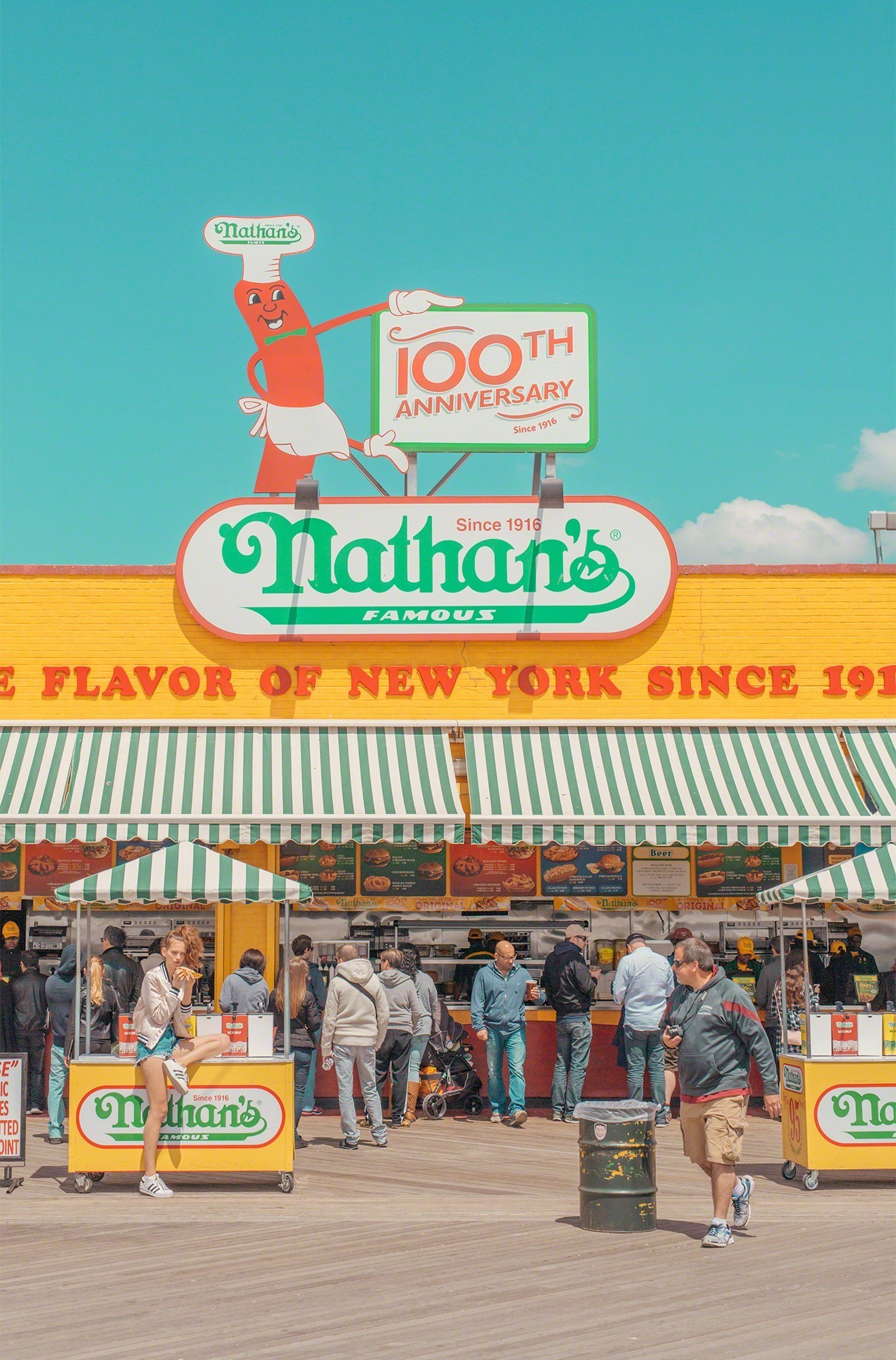 A group of people standing in front of a Nathan's hot dog stand.