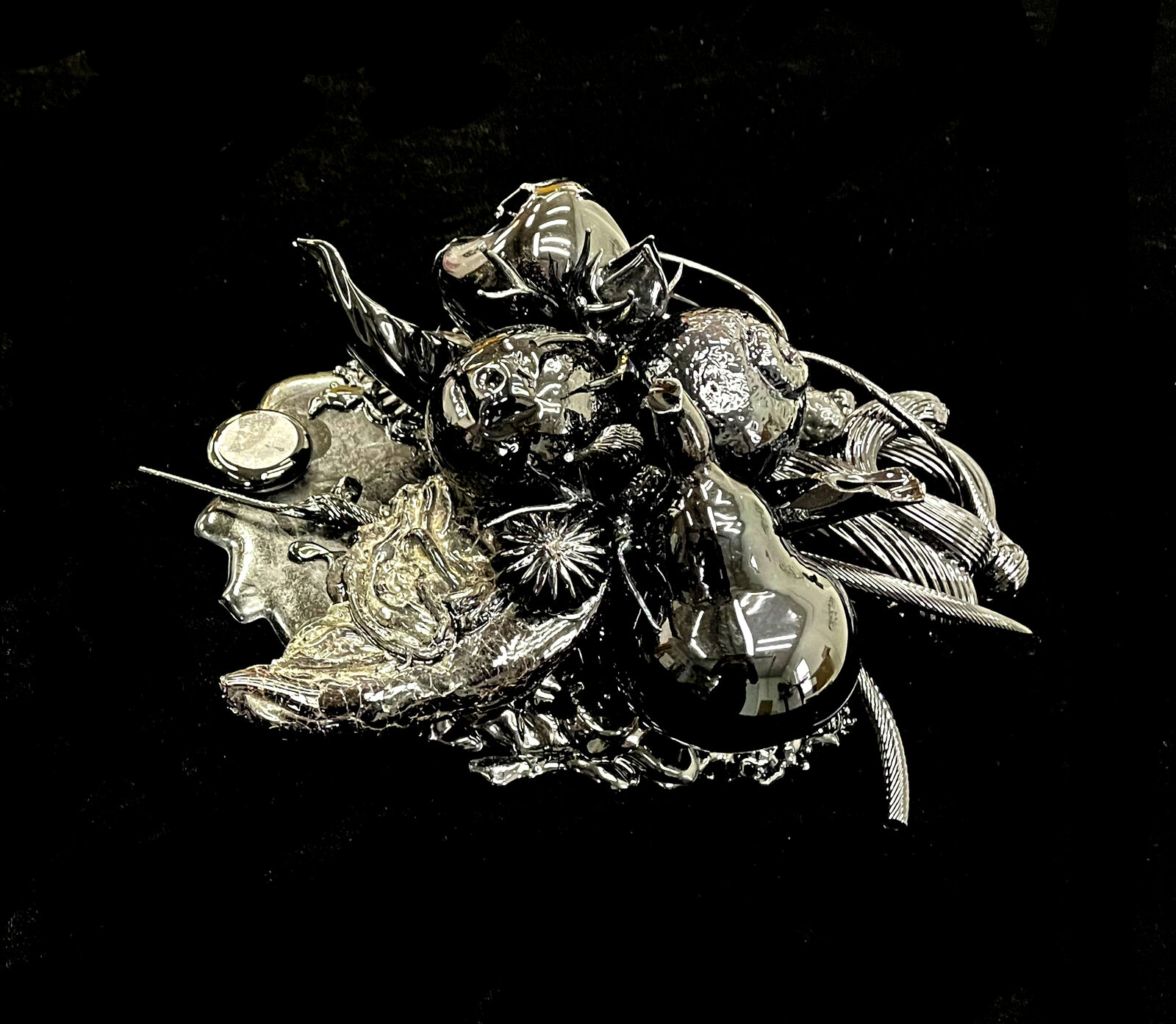 A complex silver brooch featuring a chaotic arrangement of insects, flowers, and abstract shapes.