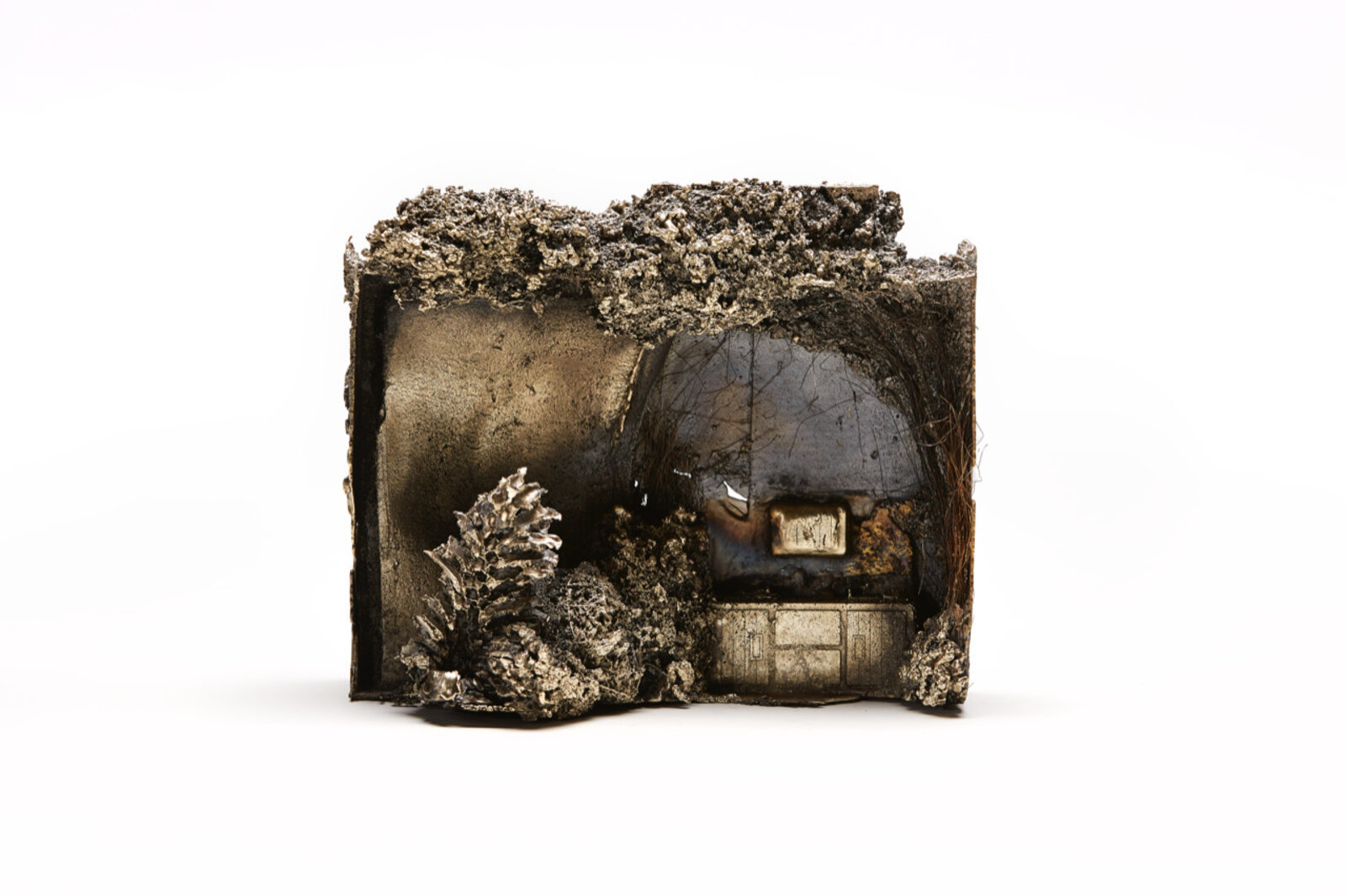 A miniature diorama of a scorched interior with a burnt pinecone and charred furniture.