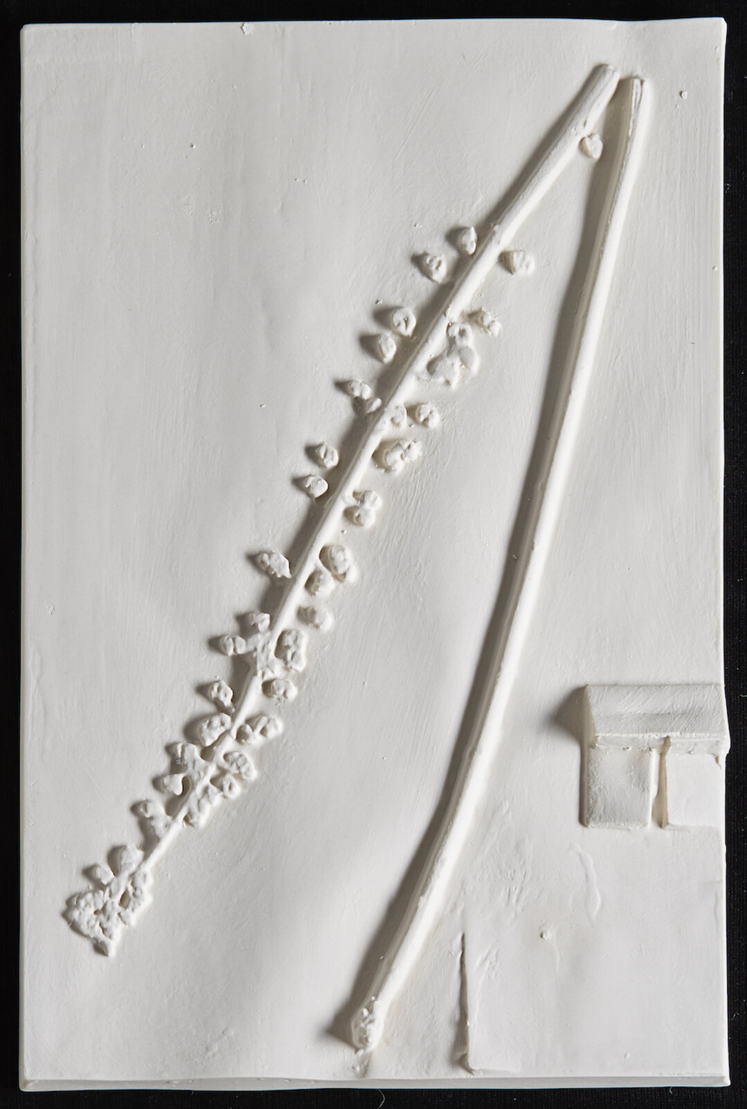 A white relief sculpture featuring a diagonal branch with small buds and a simple bench.