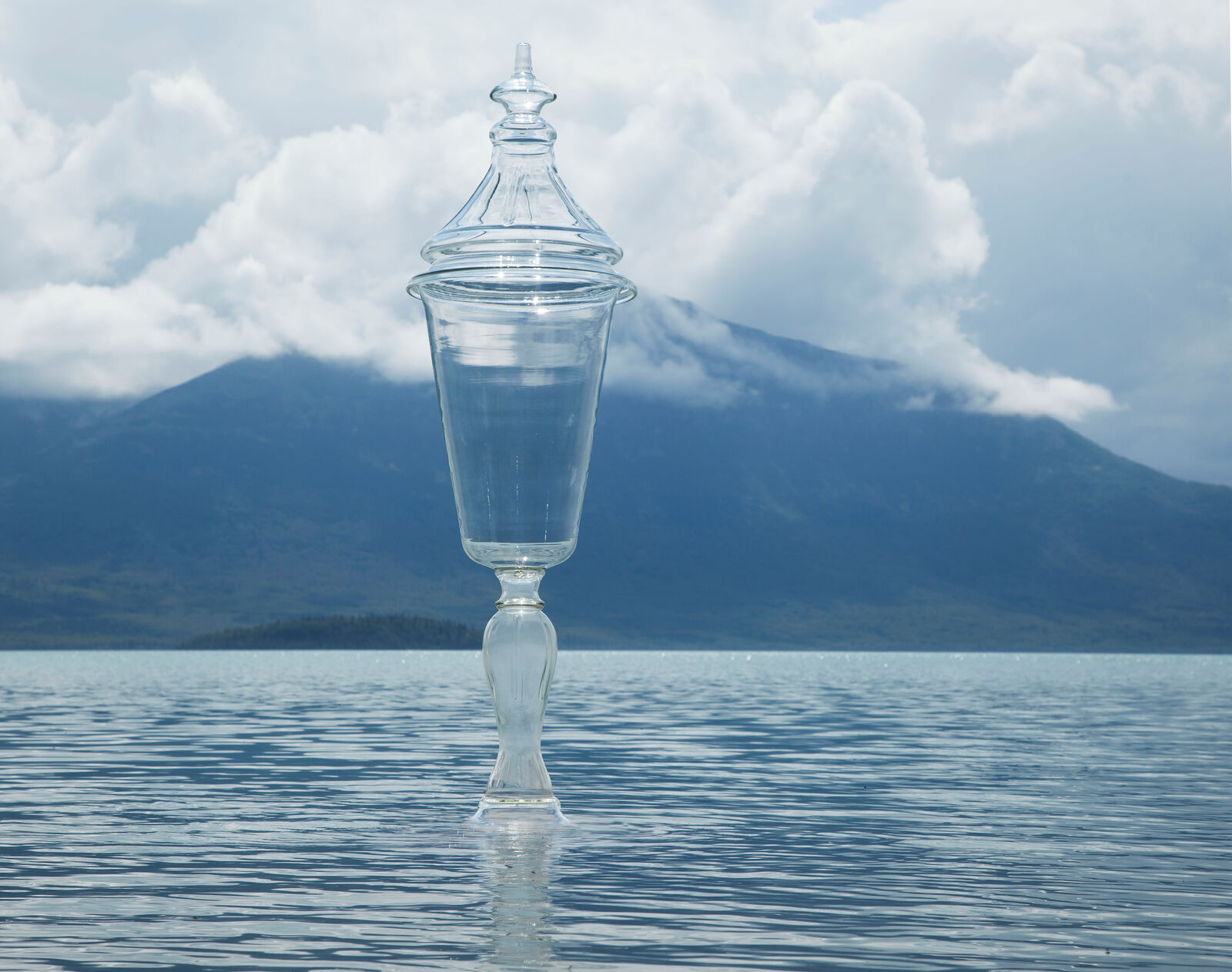 A solitary glass urn floats serenely on a calm lake with mountains in the background.