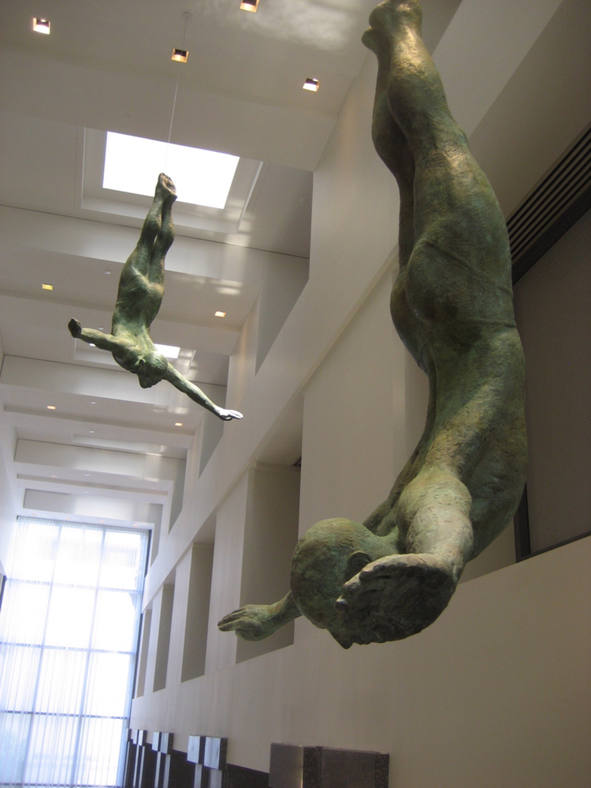 Two bronze figures appear to be floating or diving in mid-air against a stone wall.