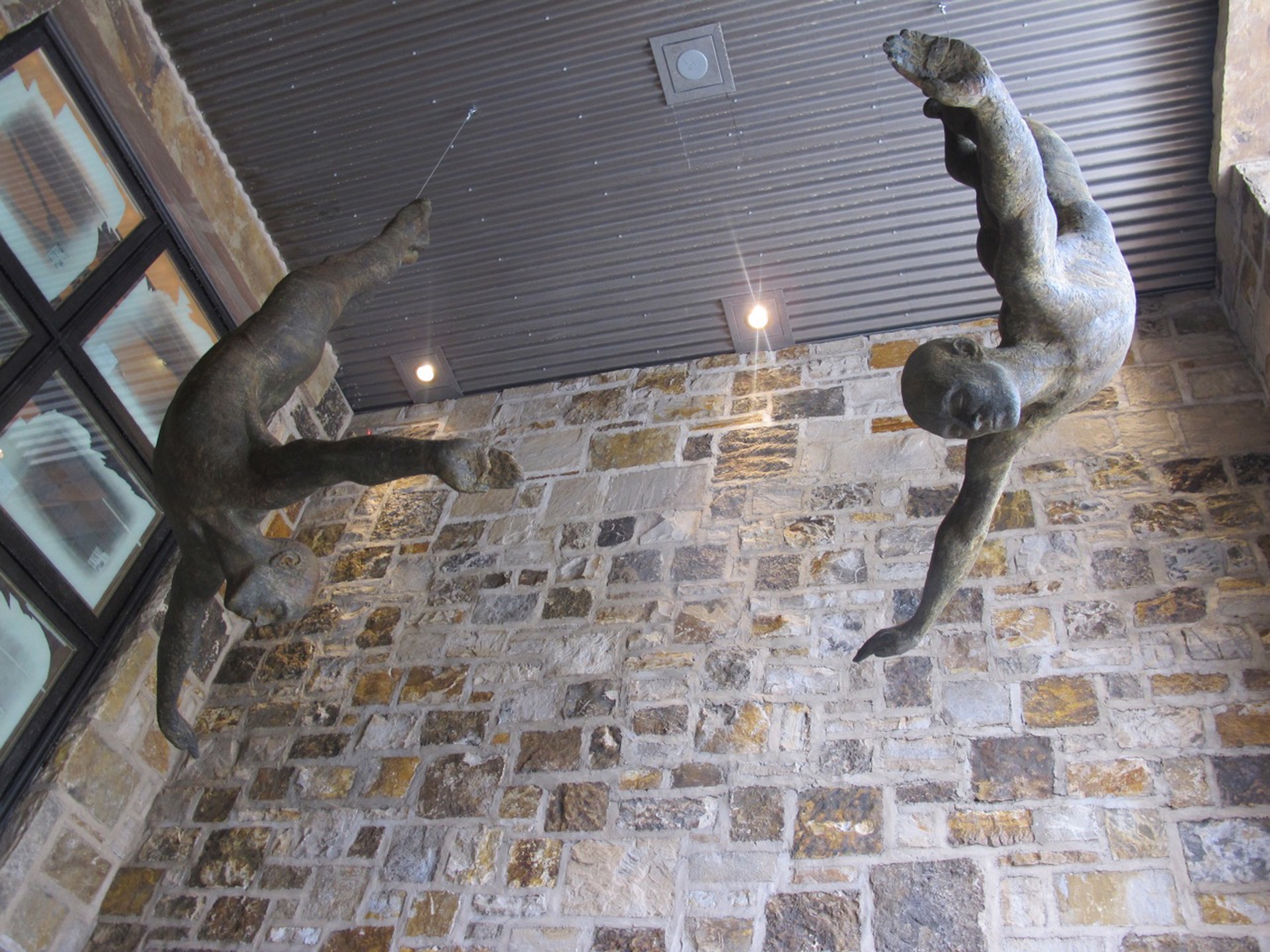 Two bronze figures appear to be floating or diving in mid-air against a stone wall.