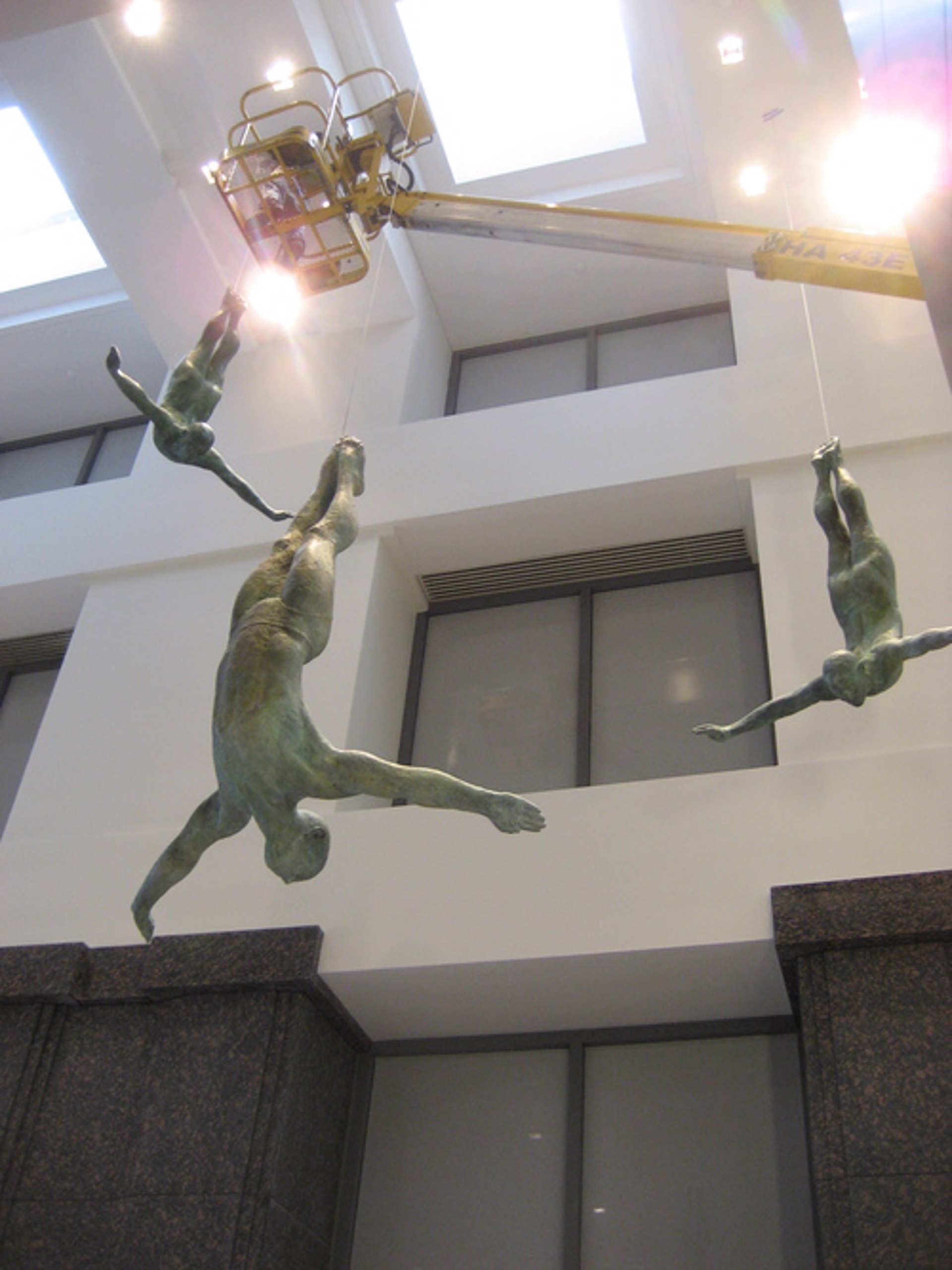 Two bronze figures appear to be floating or diving in mid-air against a stone wall.