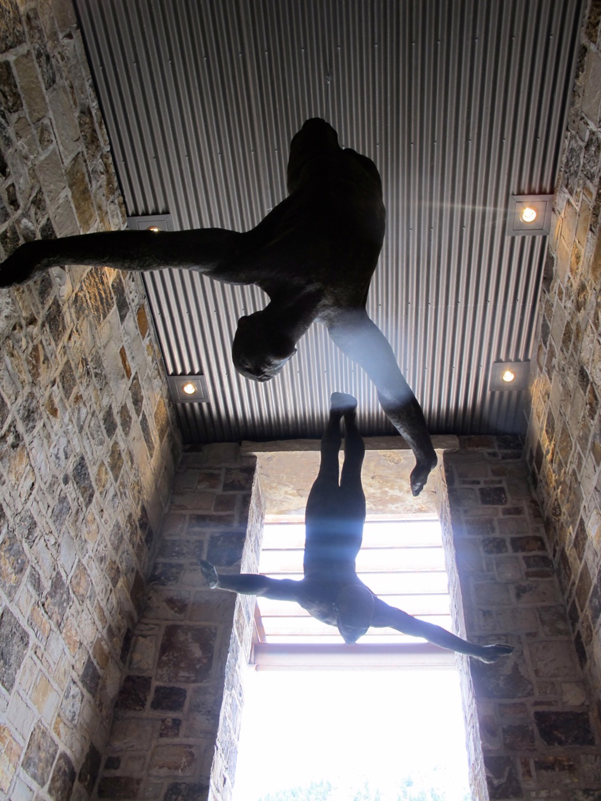 Two bronze figures appear to be floating or diving in mid-air against a stone wall.
