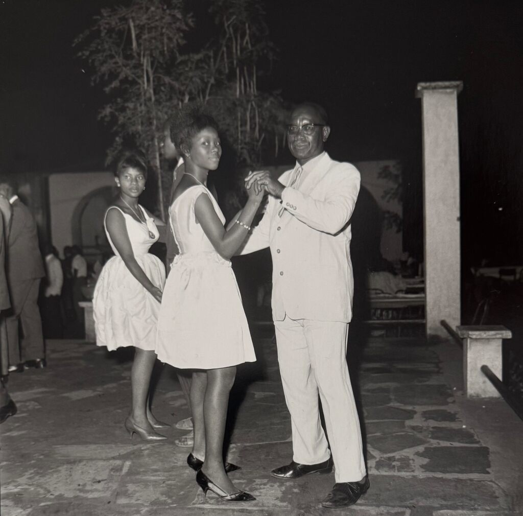 A black-and-white photograph captures a couple dancing at an evening social gathering.