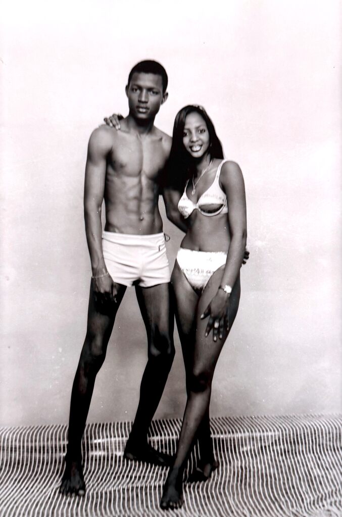 A black-and-white studio portrait of a man and woman in swimwear posing together.