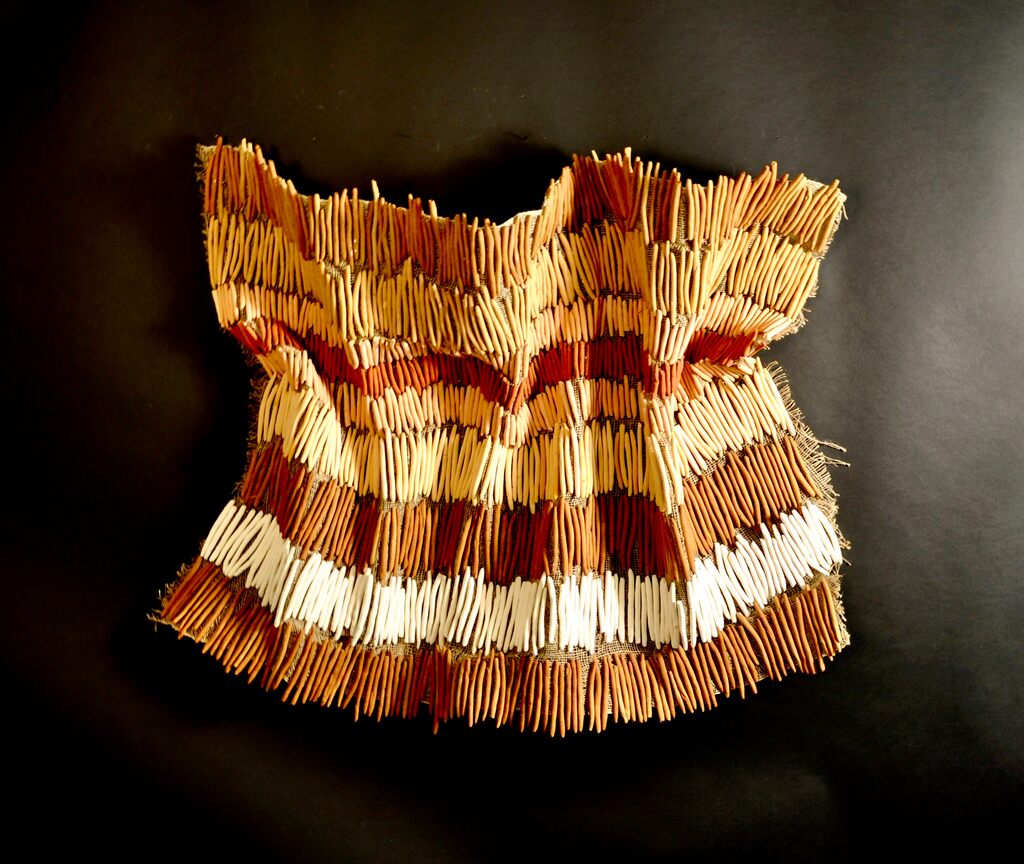 A textured, sleeveless garment made from numerous thin wooden sticks arranged in horizontal bands.
