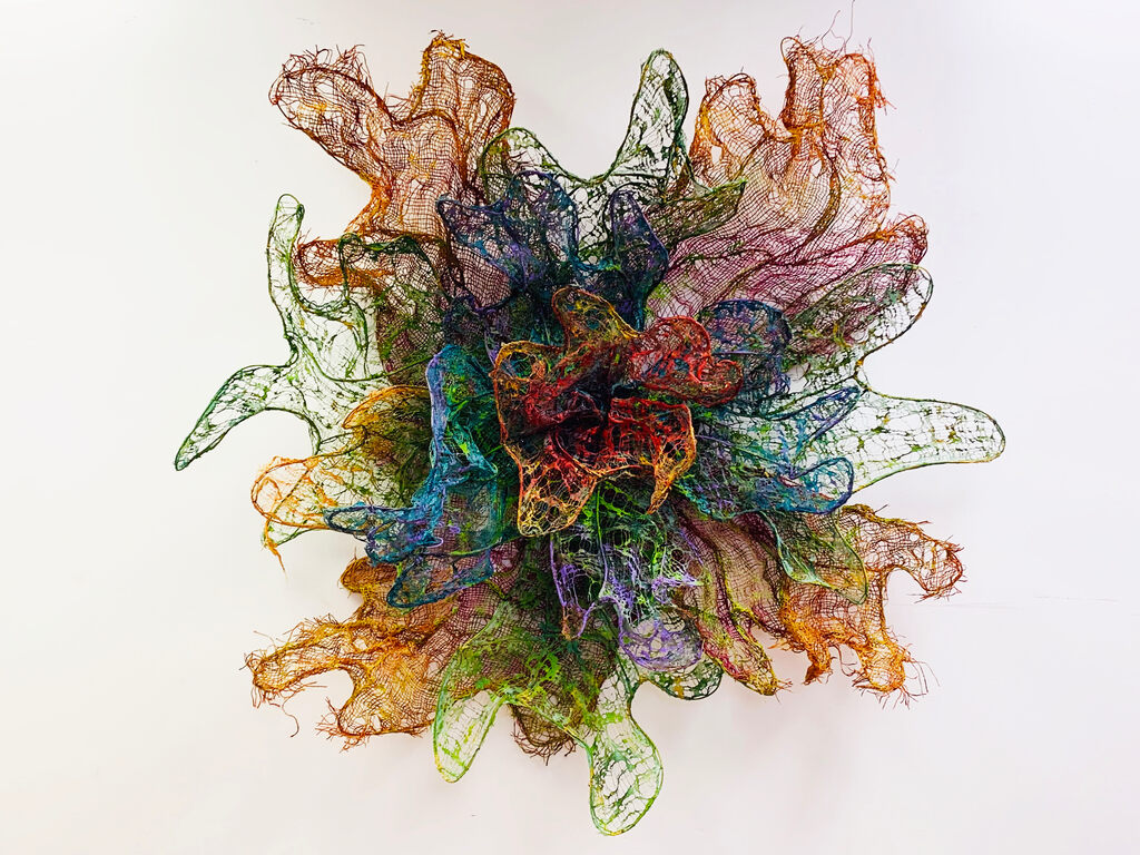 A colorful, multi-layered wire sculpture resembling a blooming flower against a plain background.