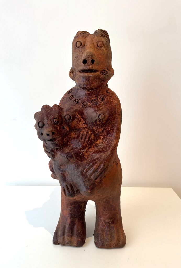 A rustic terracotta sculpture of a standing figure holding a smaller companion.