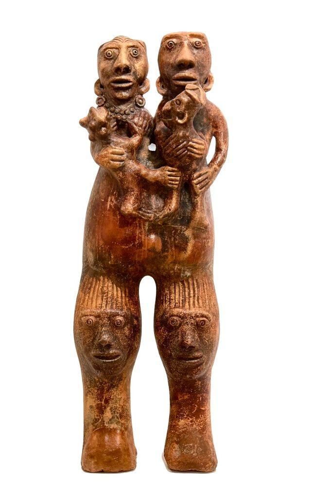 A dual-headed clay sculpture with four faces and two small figures held in the arms.