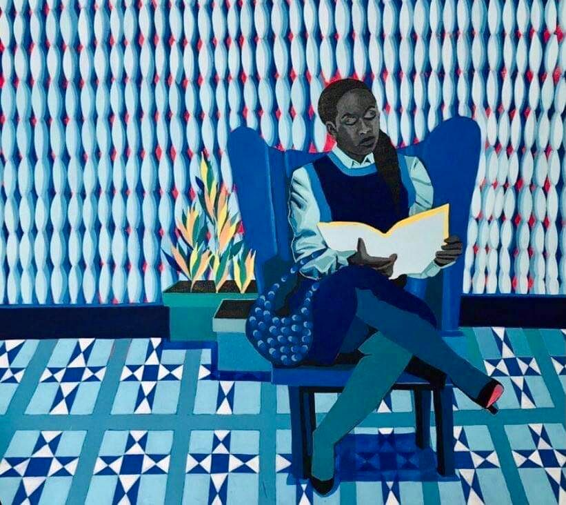 A person sits in a blue chair reading a book against a patterned wall.