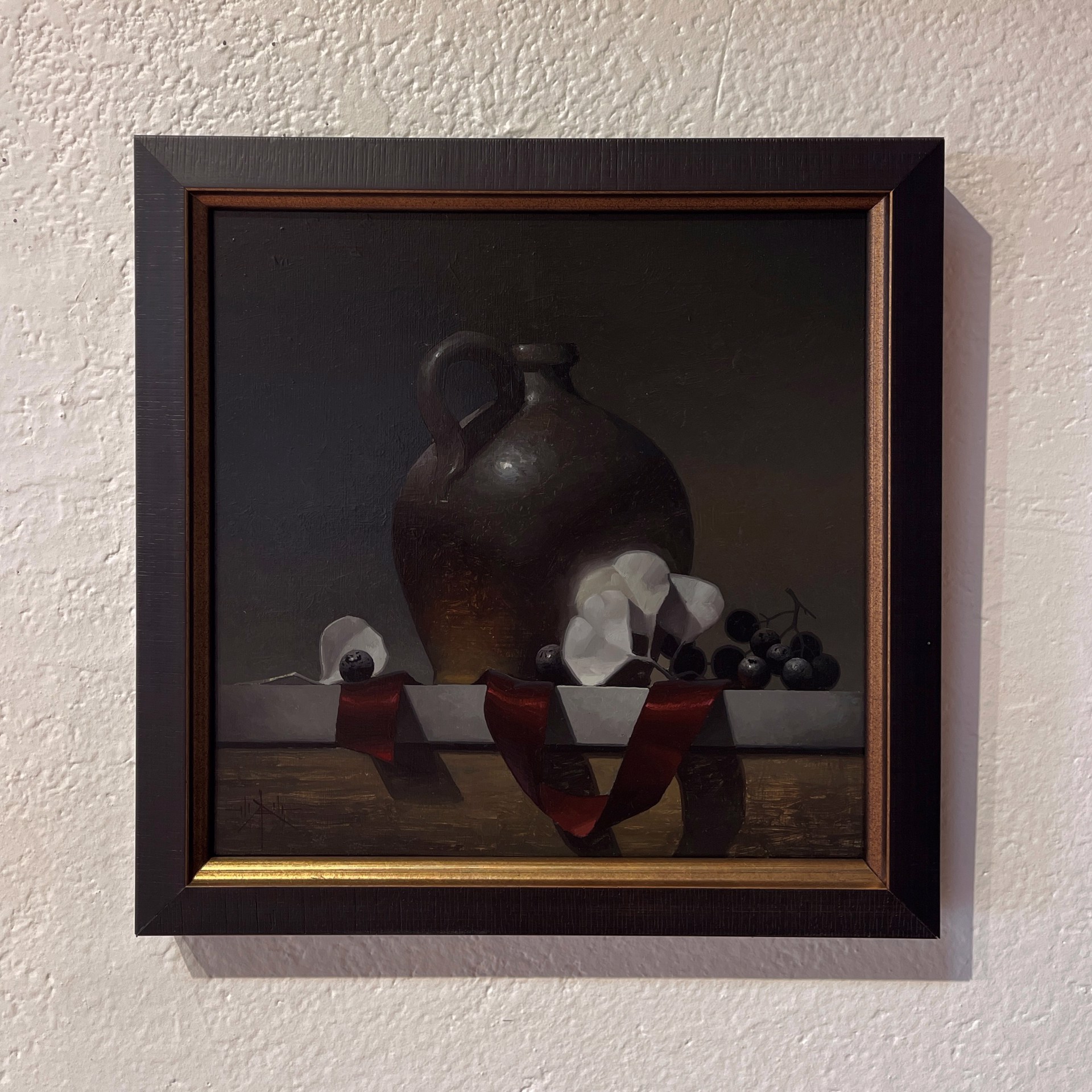 A dark still life featuring a ceramic jug, white flowers, and grapes on a ribbon-draped ledge.