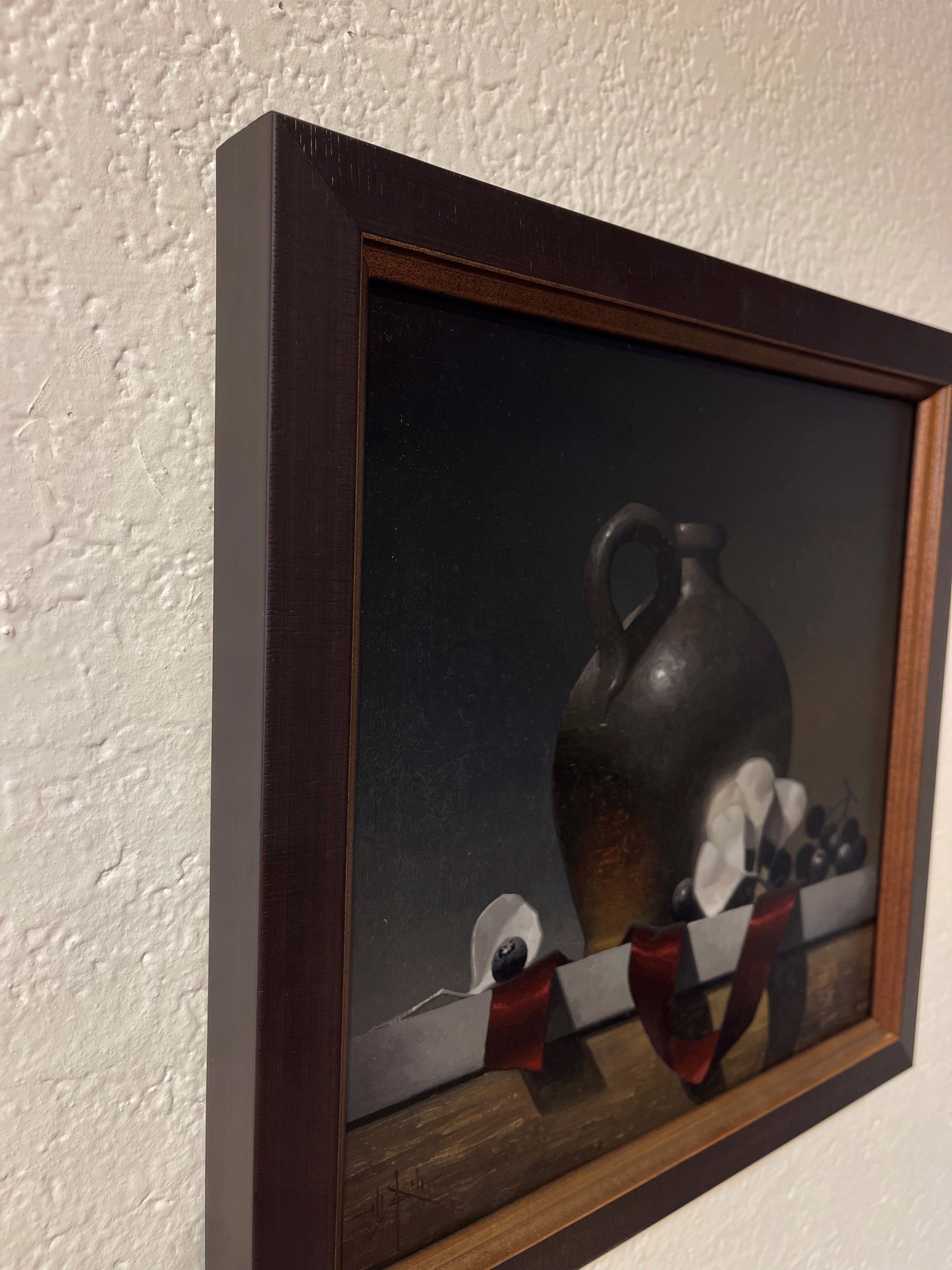 A dark still life featuring a ceramic jug, white flowers, and grapes on a ribbon-draped ledge.