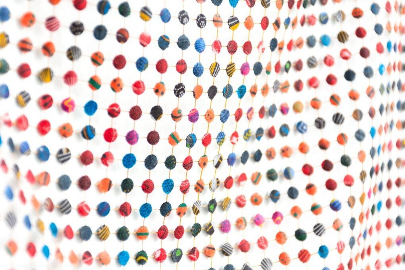 A colorful grid of small, patterned spheres arranged in a wavy formation against a stark white background.