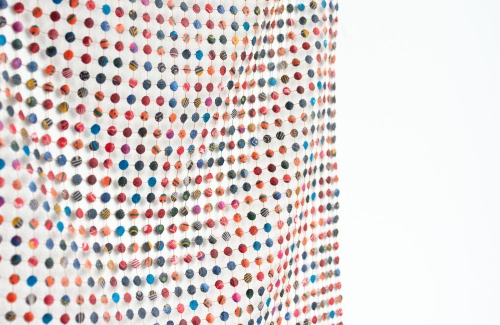 A colorful grid of small, patterned spheres arranged in a wavy formation against a stark white background.