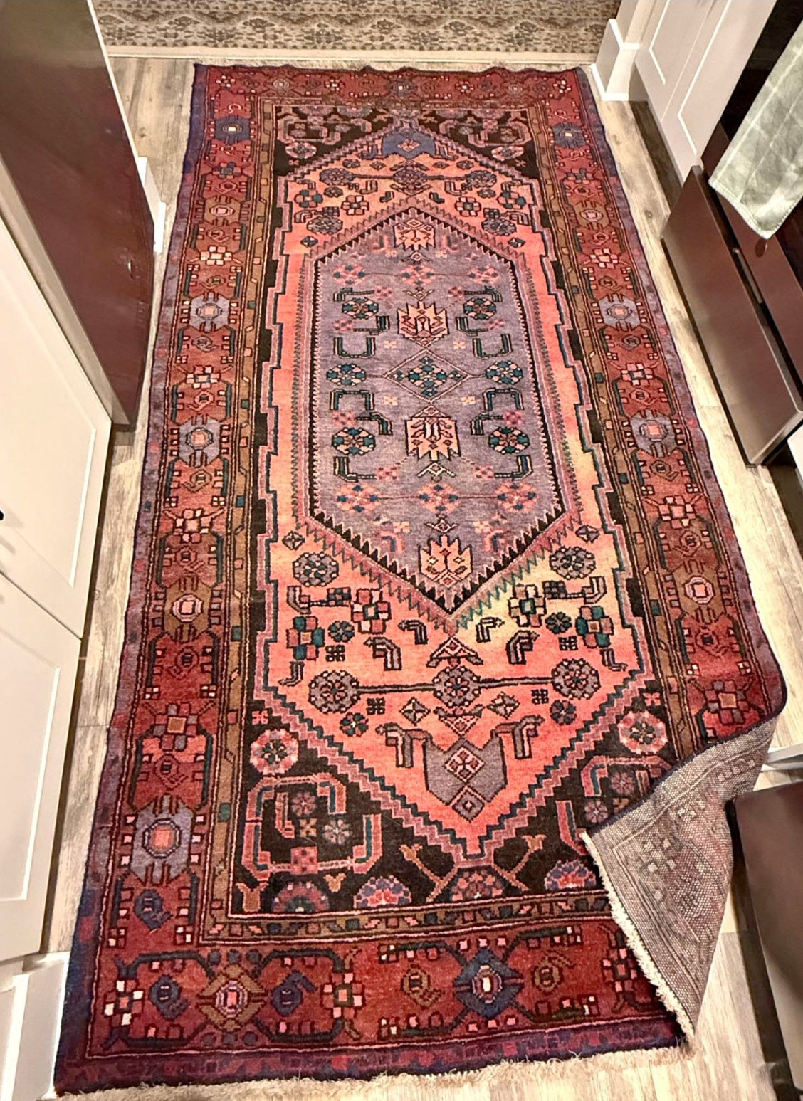 A traditional runner rug with a central medallion design, featuring geometric patterns and a rich palette of reds, purples, and blues.