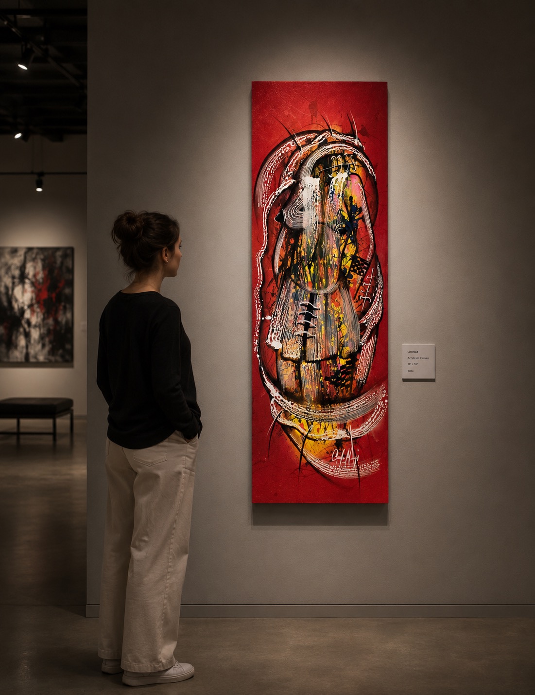 A person in a black shirt and light pants stands in an art gallery, gazing at a tall red canvas featuring an abstract, face-like composition with white brushstrokes.