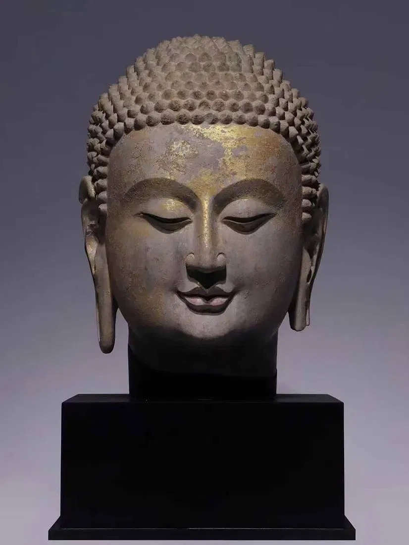 A serene stone bust with a golden forehead and a black pedestal.