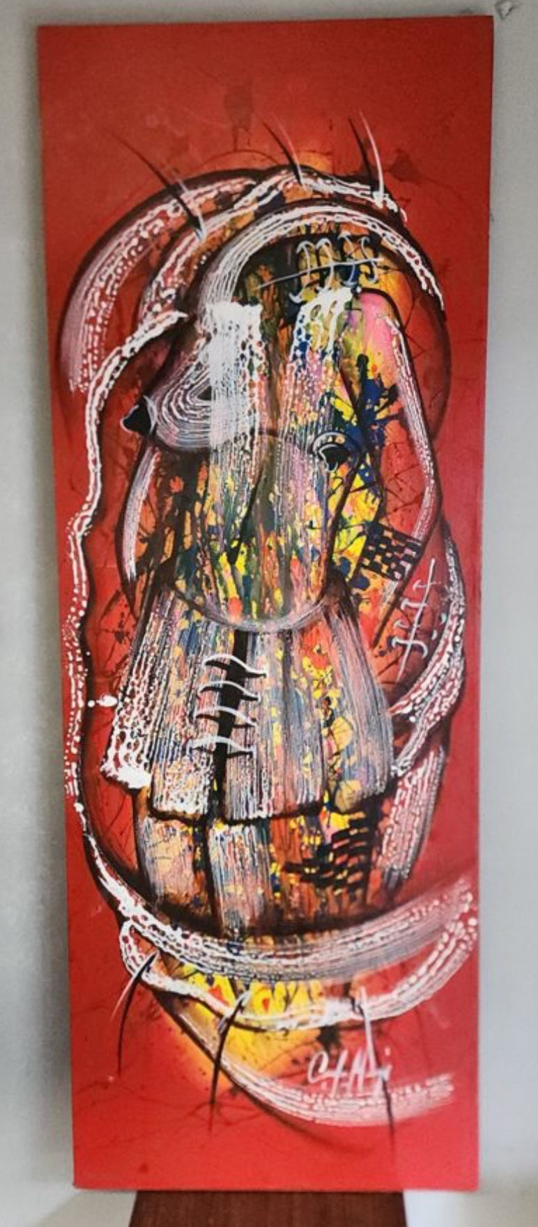 A person in a black shirt and light pants stands in an art gallery, gazing at a tall red canvas featuring an abstract, face-like composition with white brushstrokes.