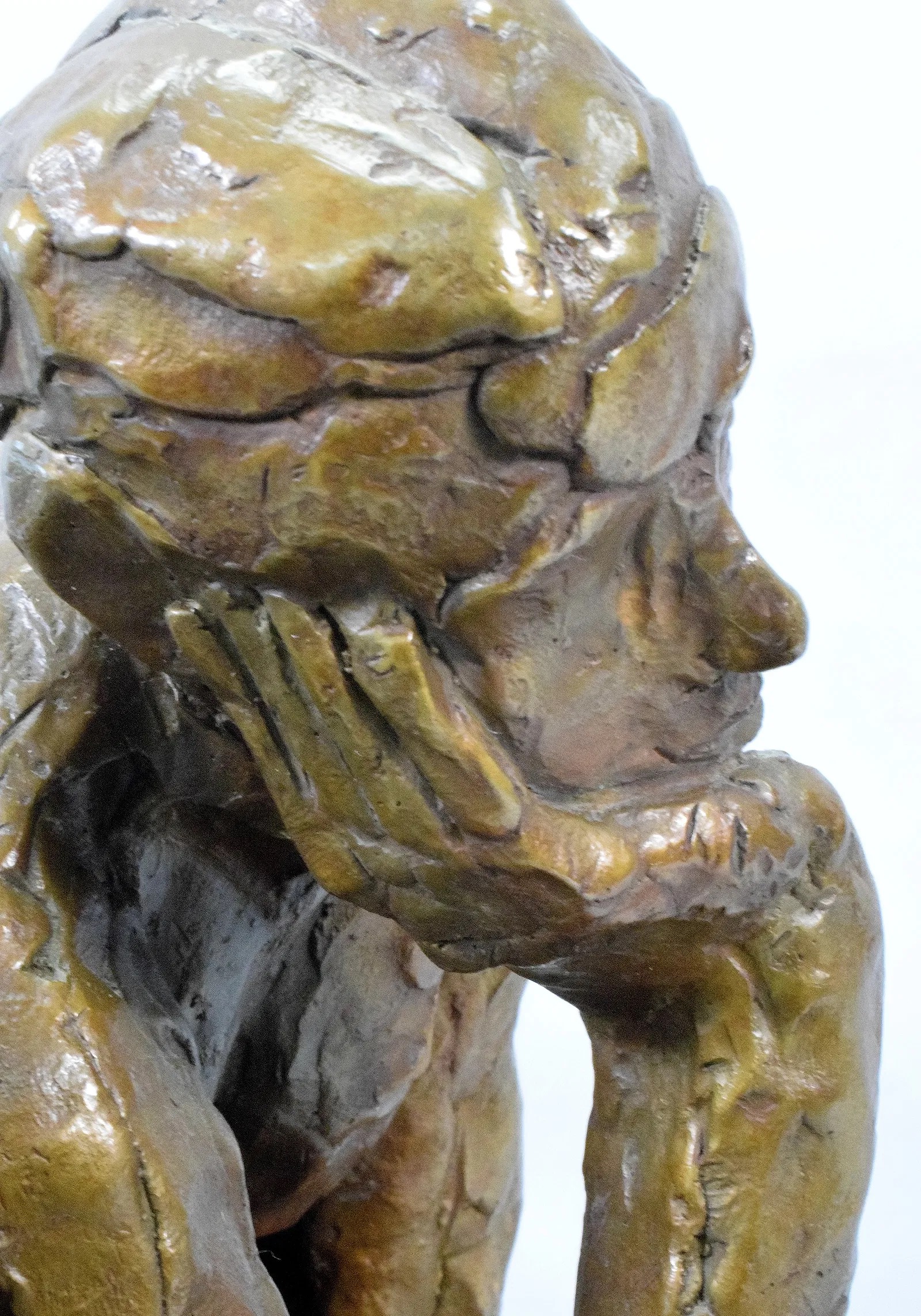 A bronze sculpture of a seated figure in deep contemplation.