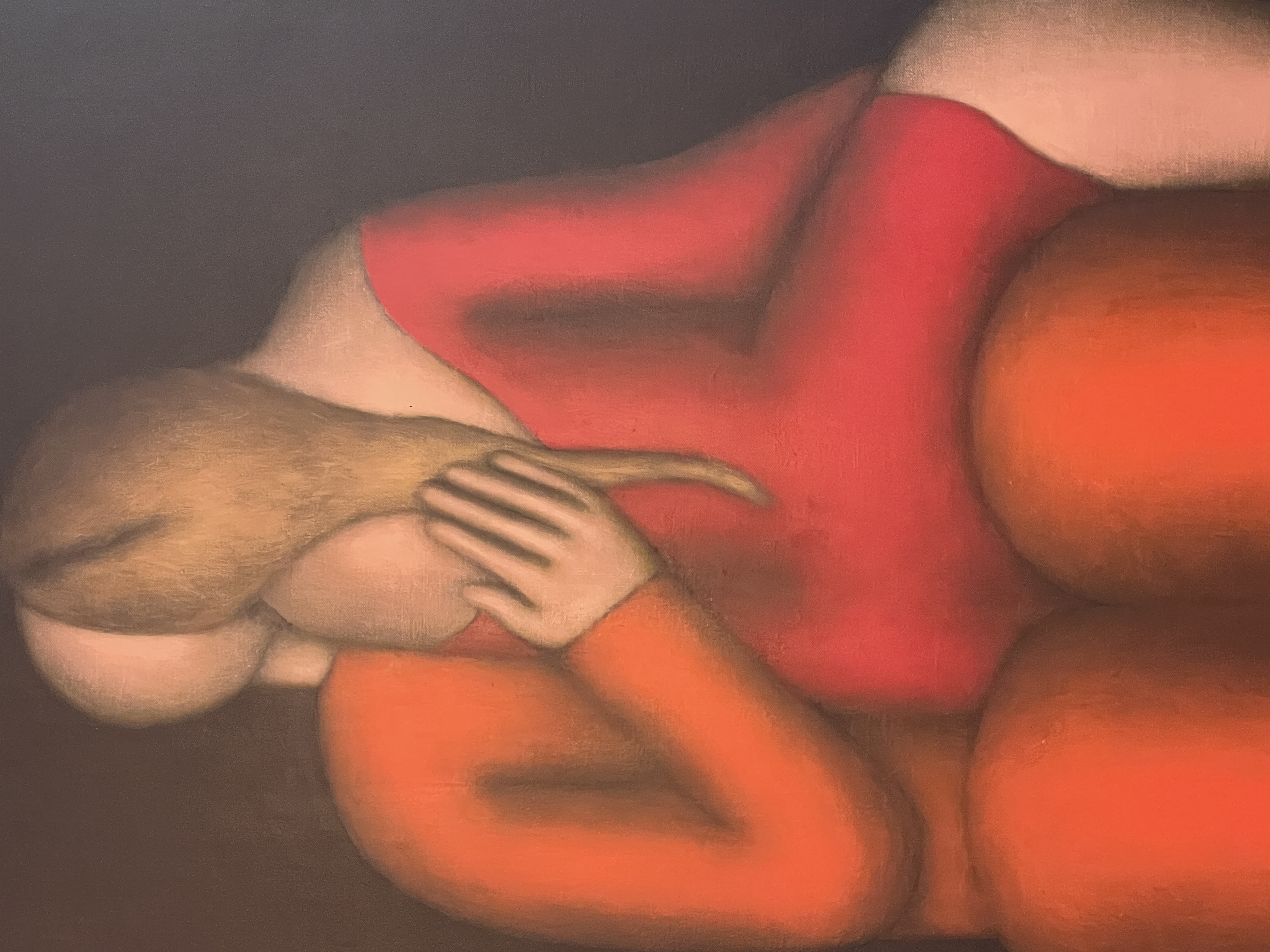 A man in a suit observes a painting of two figures embracing on red chairs.