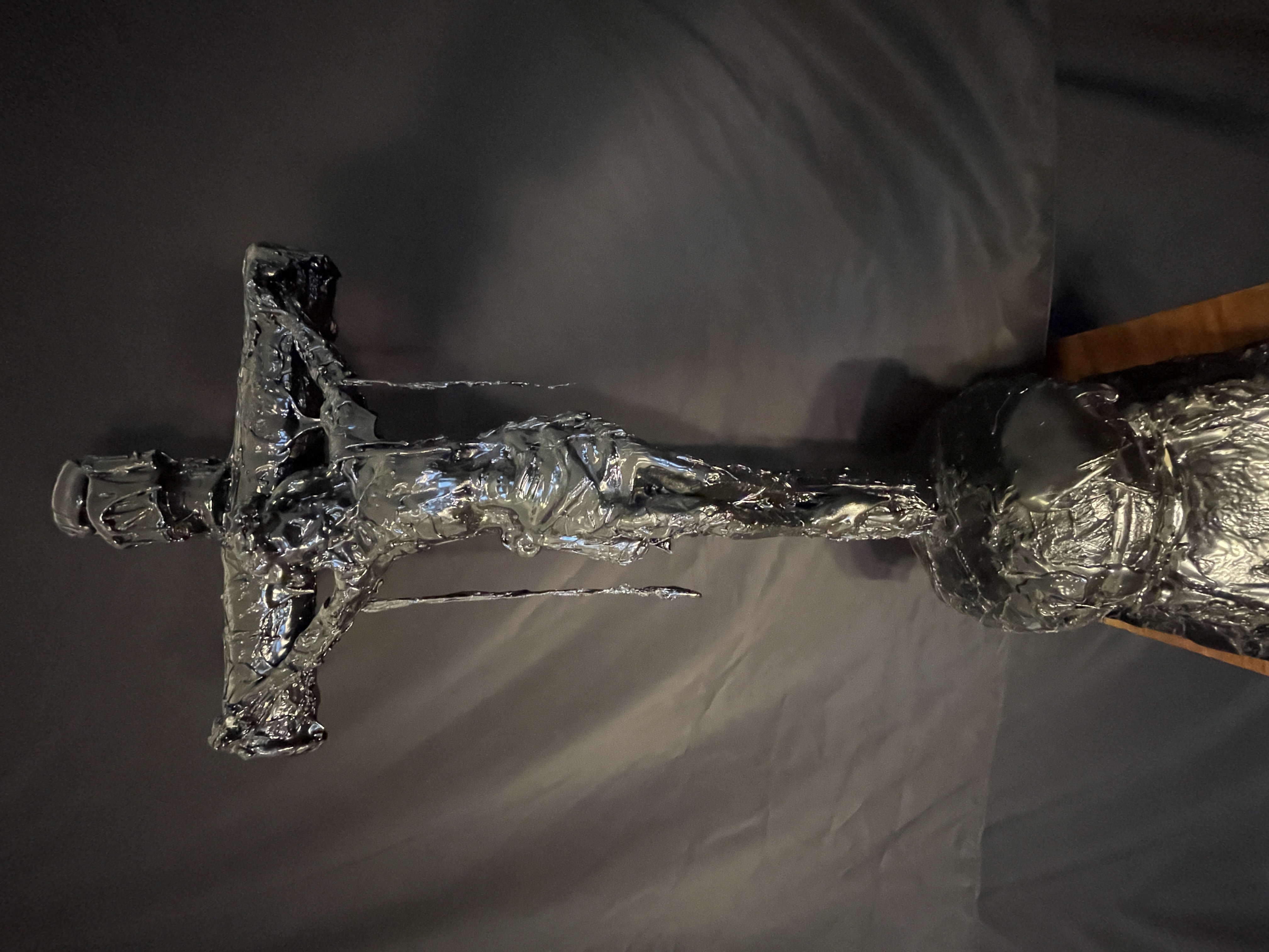 A dark, textured sculpture of a crucifixion scene displayed on a black marble pedestal.