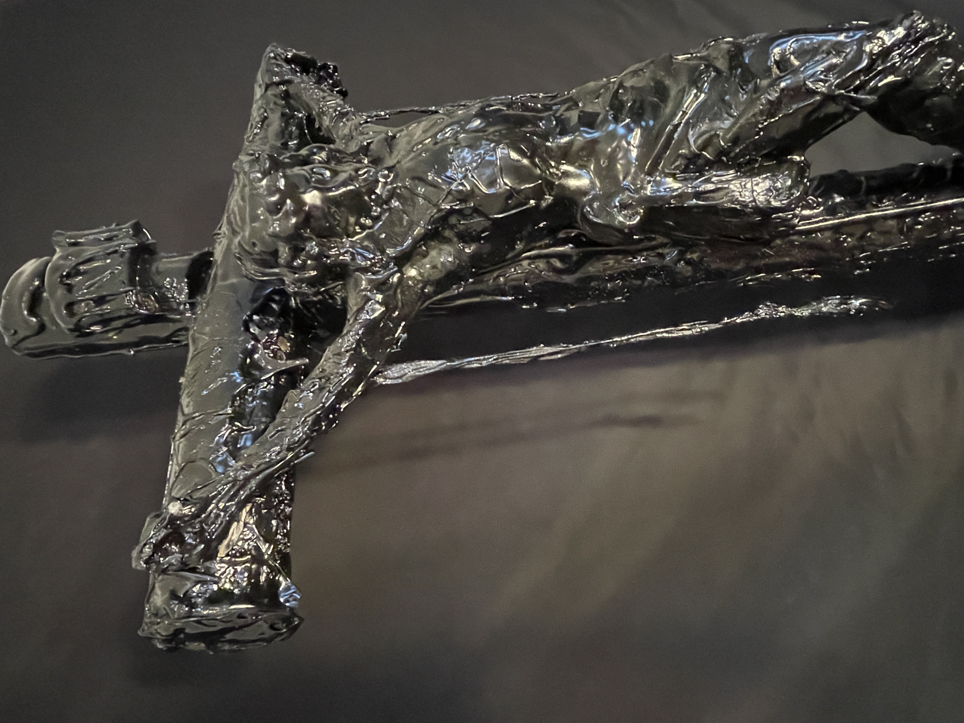 A dark, textured sculpture of a crucifixion scene displayed on a black marble pedestal.