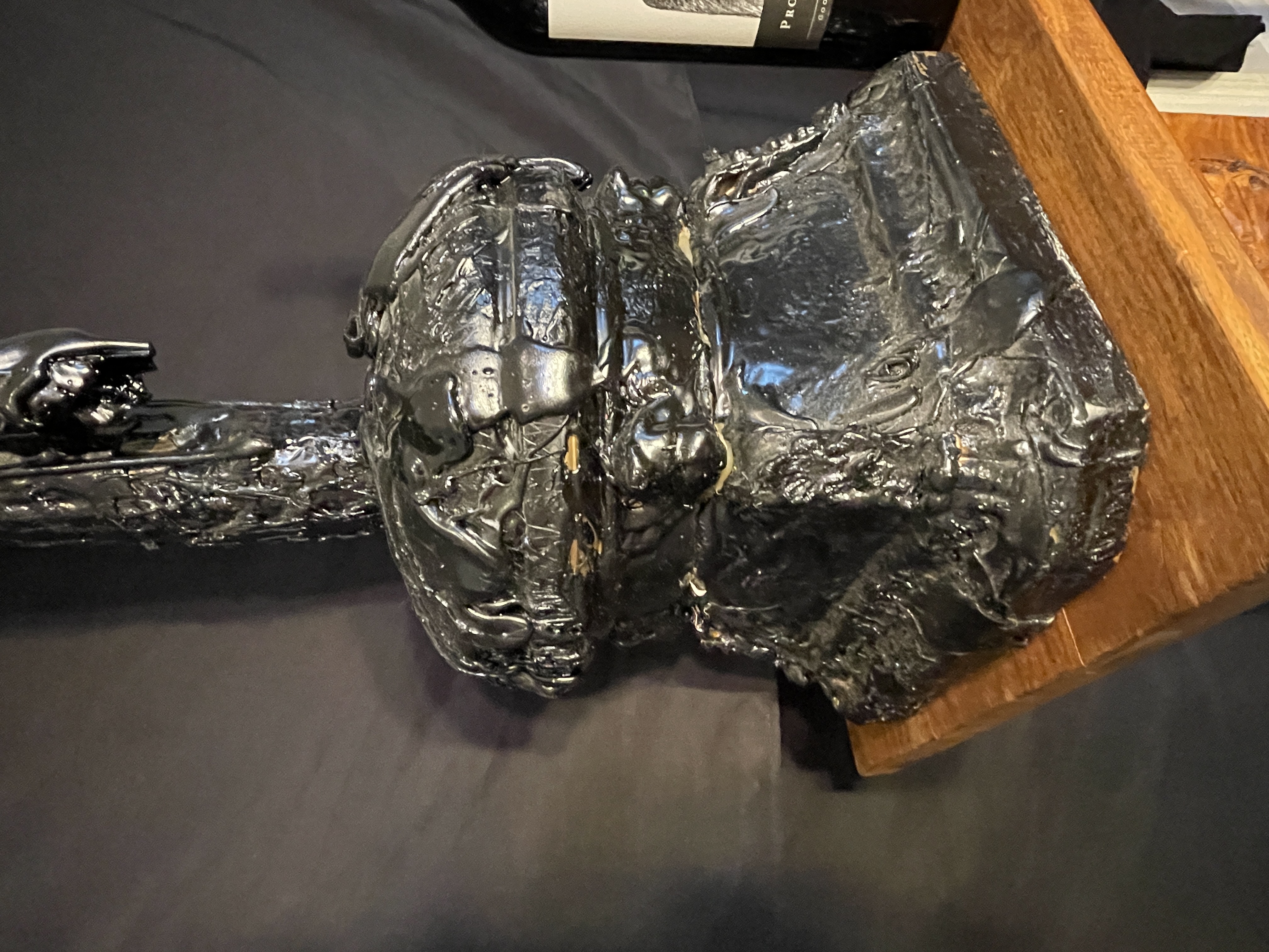 A dark, textured sculpture of a crucifixion scene displayed on a black marble pedestal.