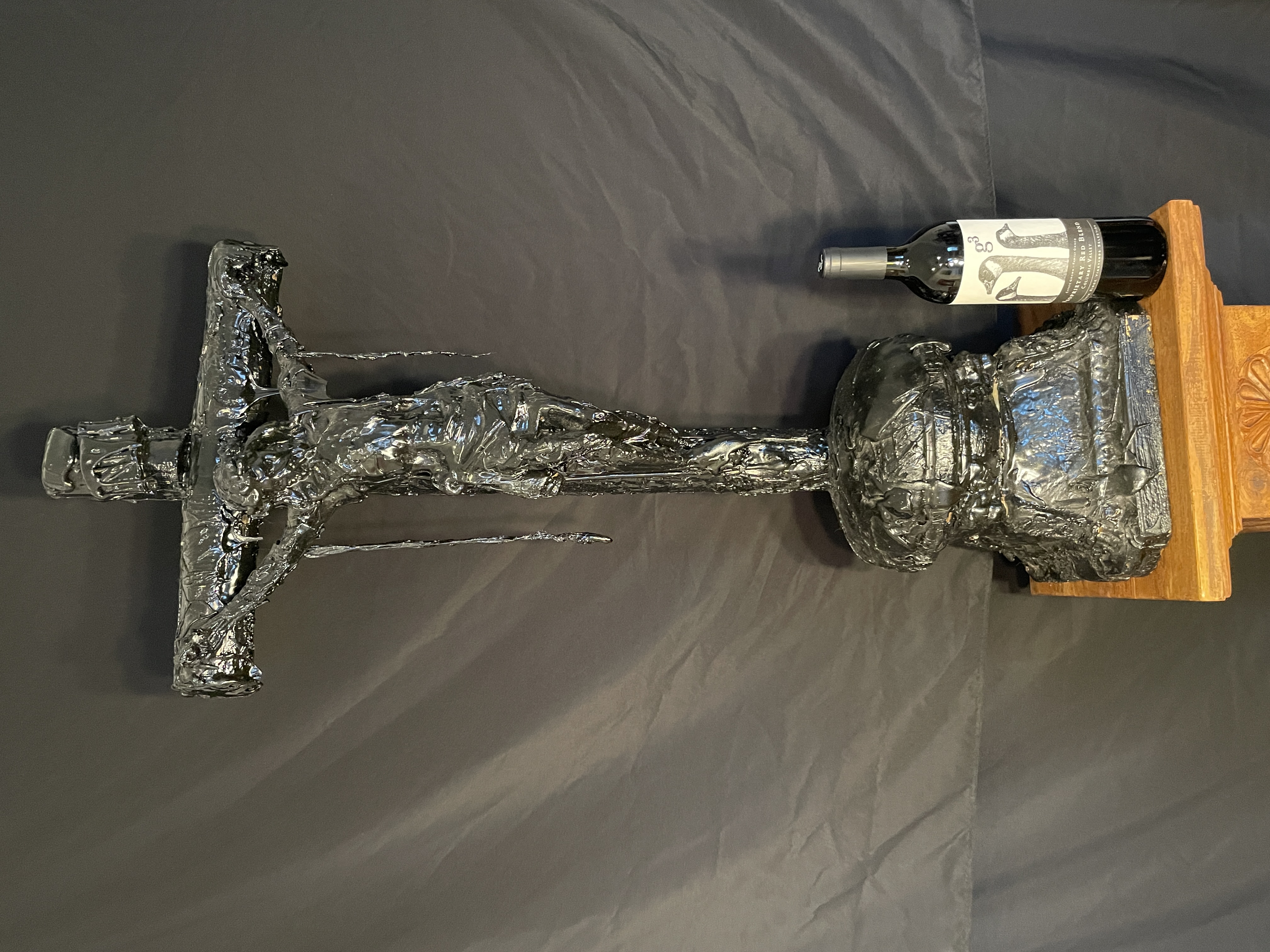A dark, textured sculpture of a crucifixion scene displayed on a black marble pedestal.