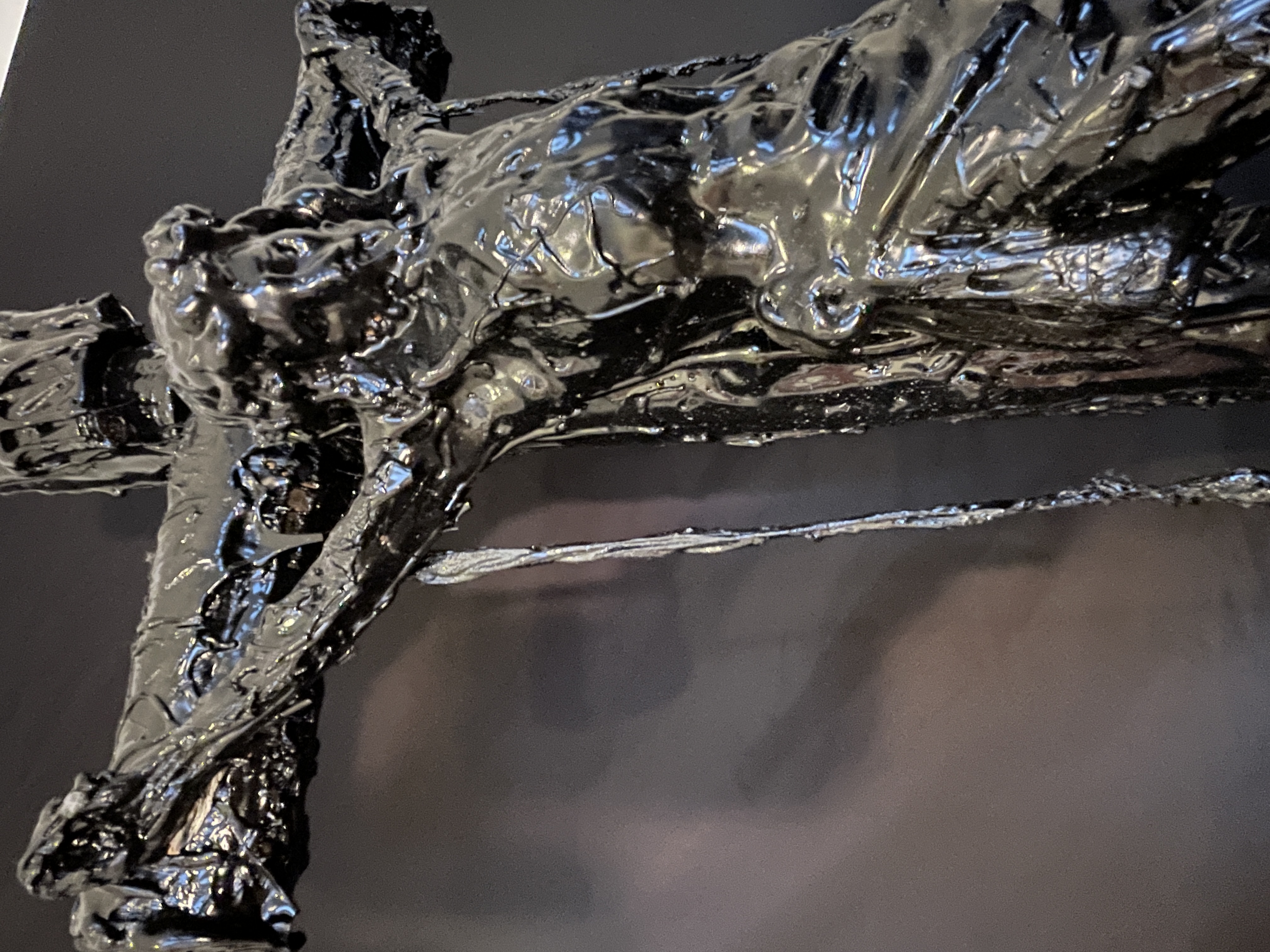 A dark, textured sculpture of a crucifixion scene displayed on a black marble pedestal.