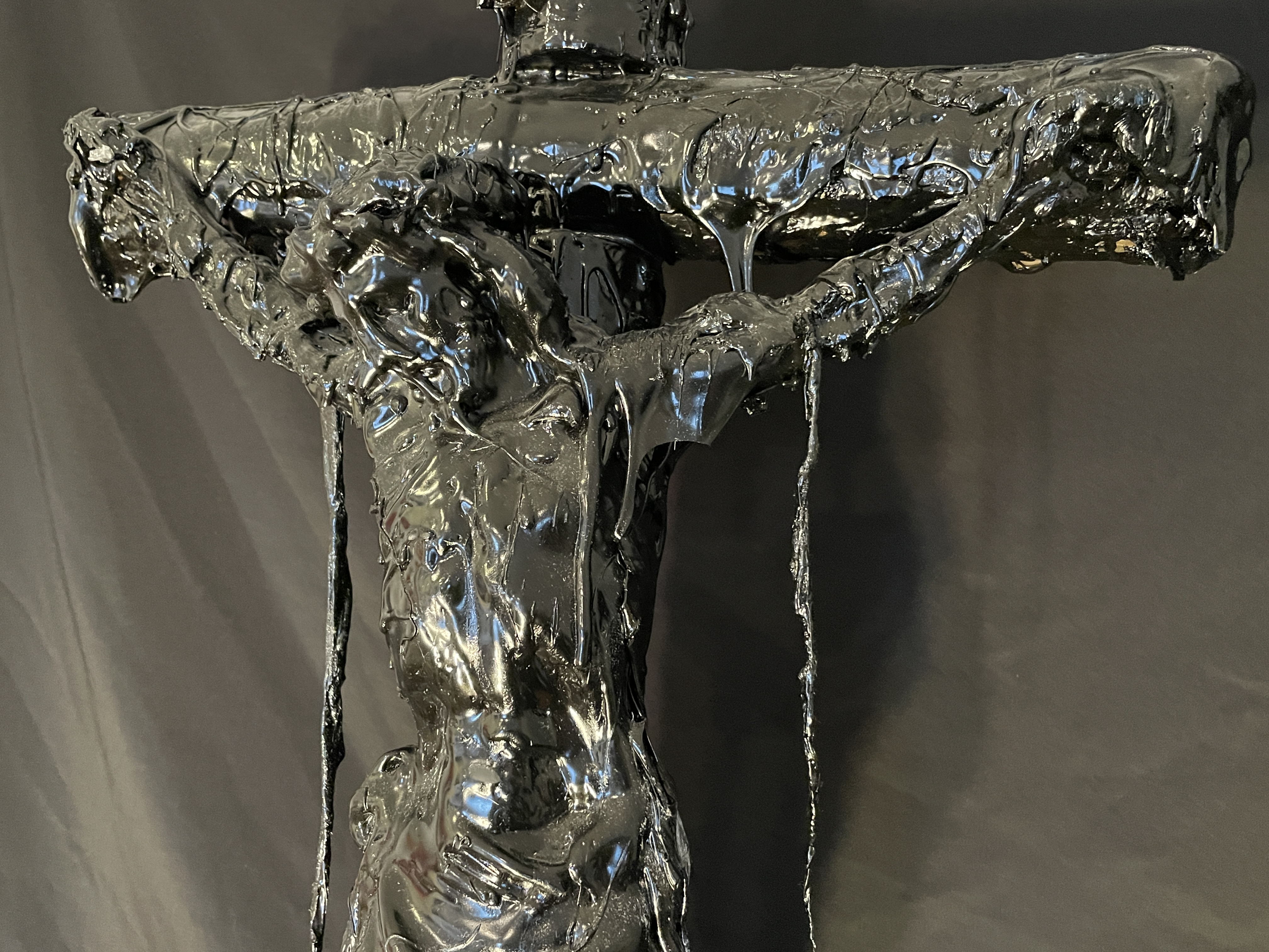 A dark, textured sculpture of a crucifixion scene displayed on a black marble pedestal.