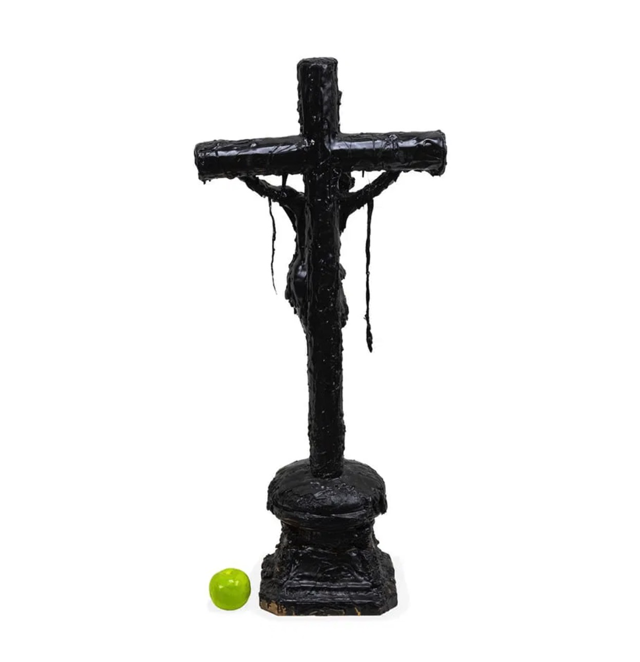 A dark, textured sculpture of a crucifixion scene displayed on a black marble pedestal.