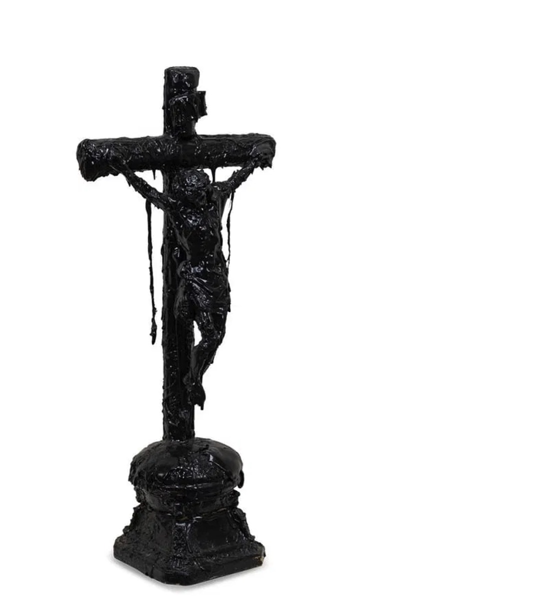 A dark, textured sculpture of a crucifixion scene displayed on a black marble pedestal.