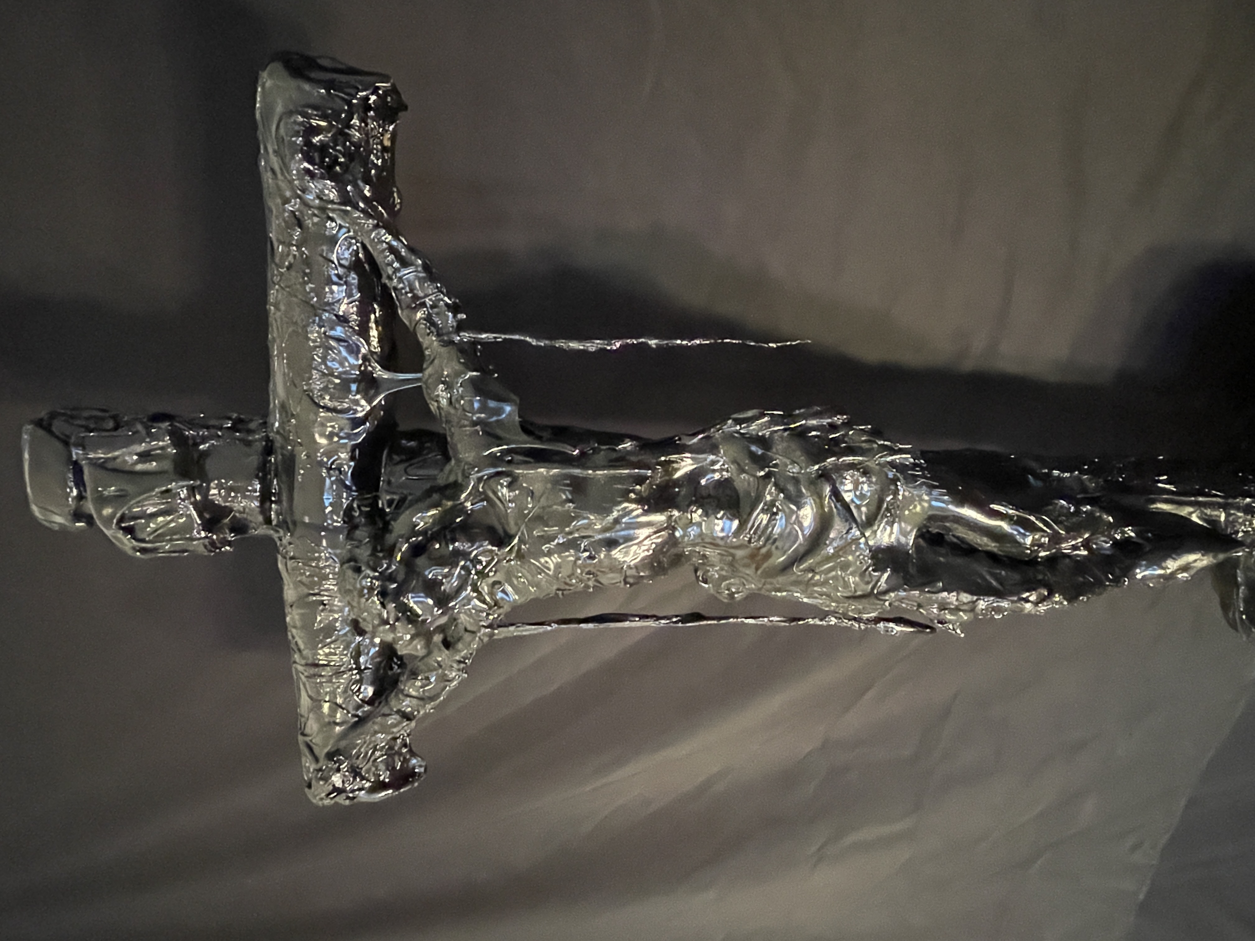 A dark, textured sculpture of a crucifixion scene displayed on a black marble pedestal.