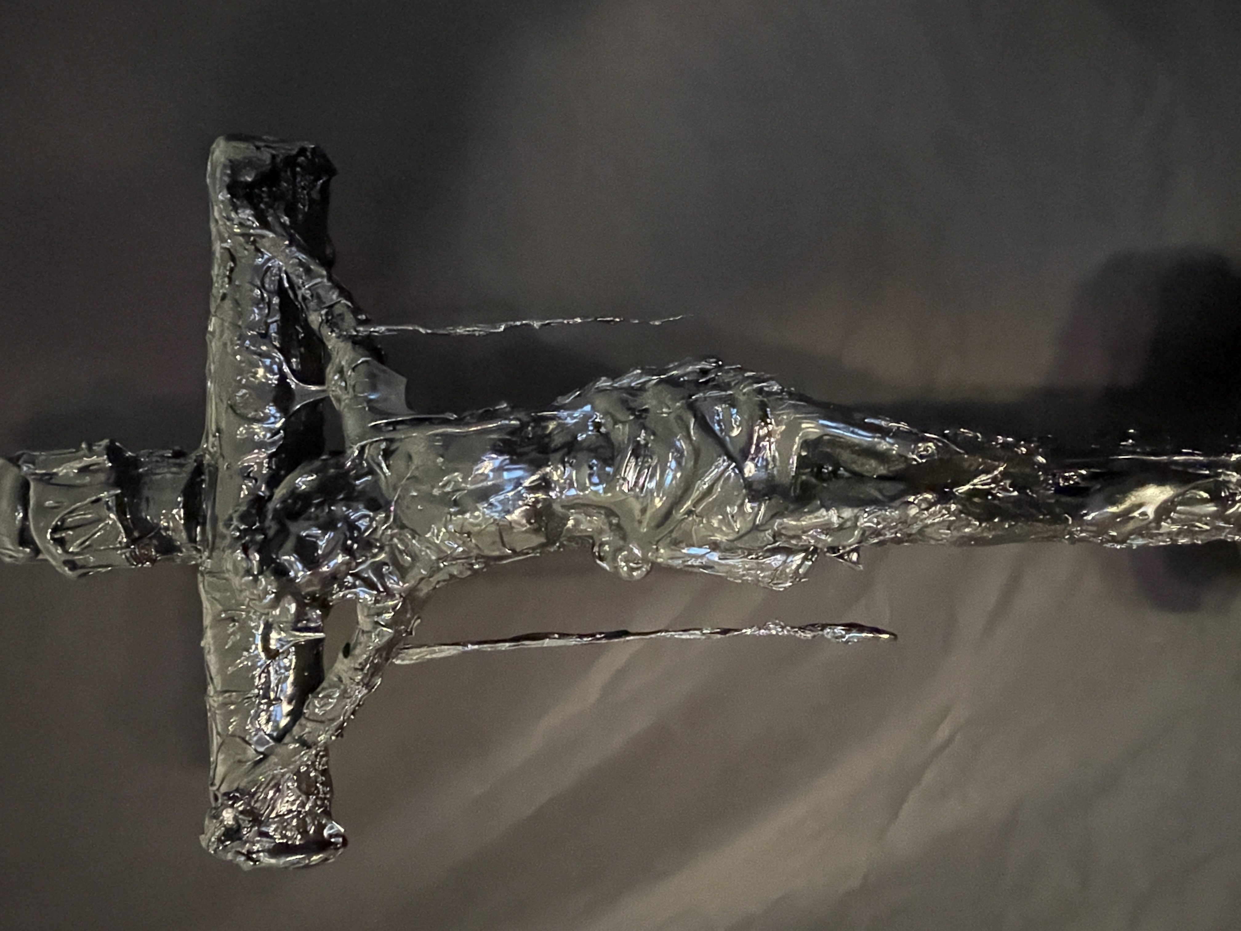 A dark, textured sculpture of a crucifixion scene displayed on a black marble pedestal.