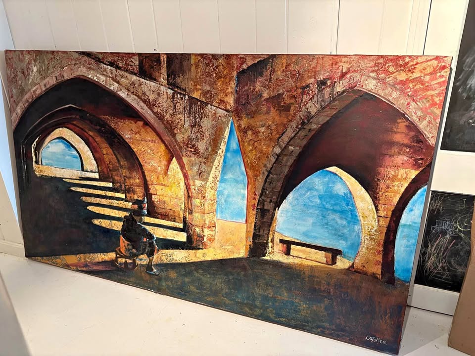 A gallery space features a large painting of an arched stone structure with a seated figure, displayed above a black bench.