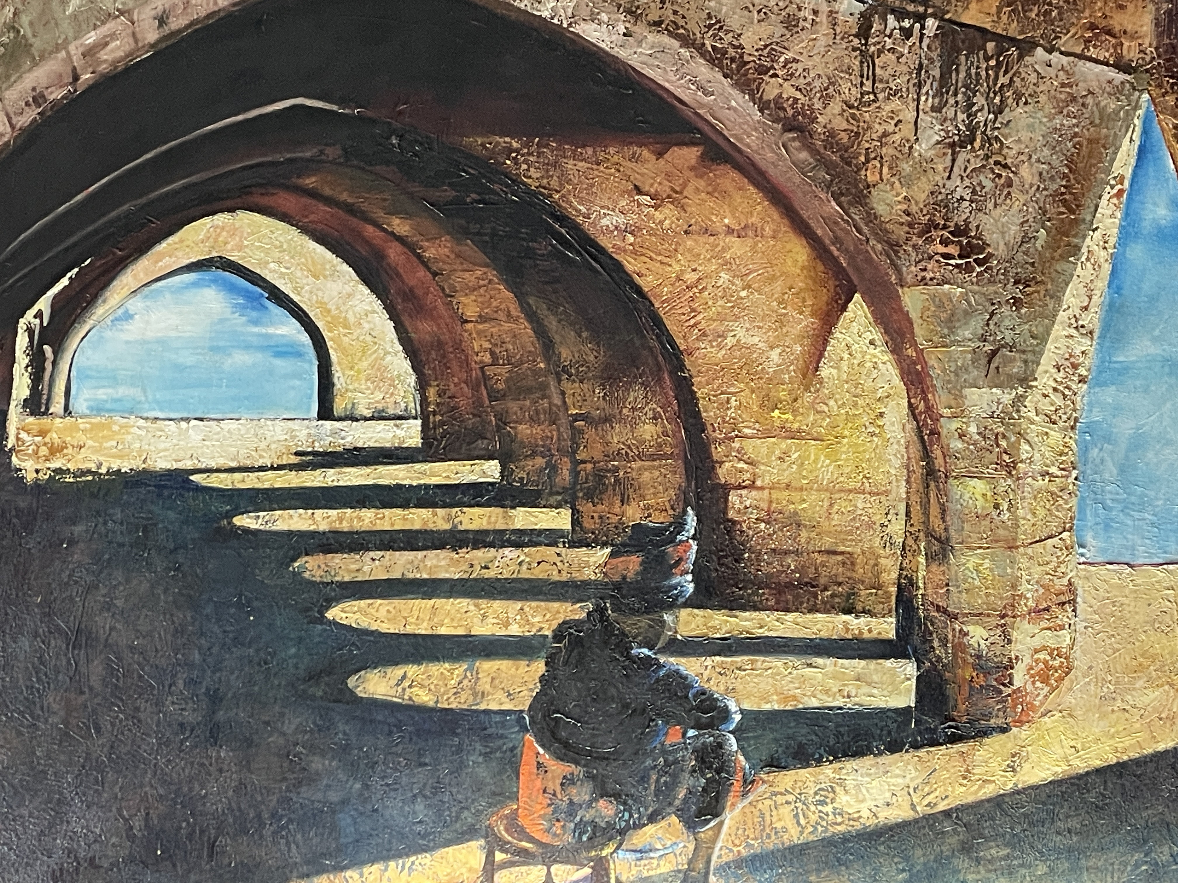 A gallery space features a large painting of an arched stone structure with a seated figure, displayed above a black bench.