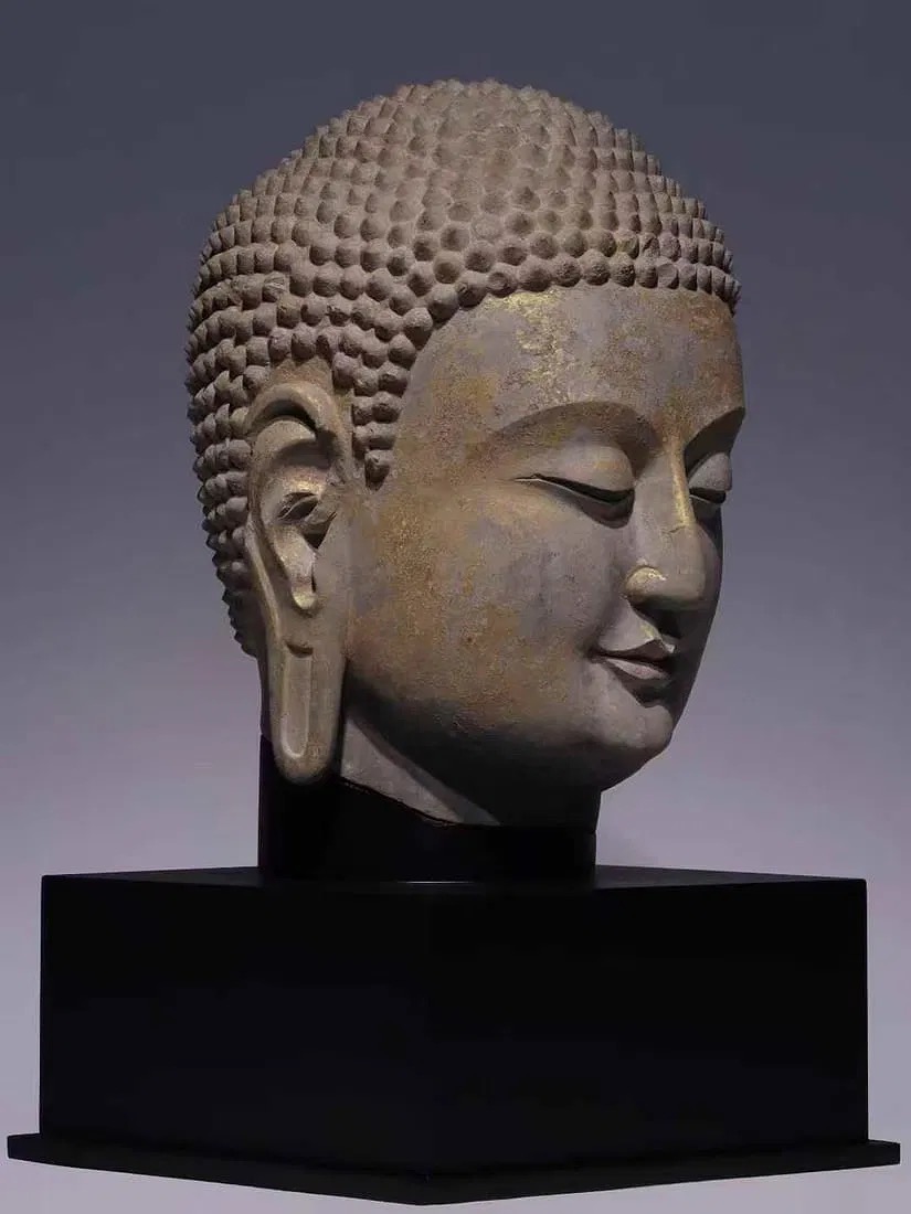 A serene stone bust with a golden forehead and a black pedestal.