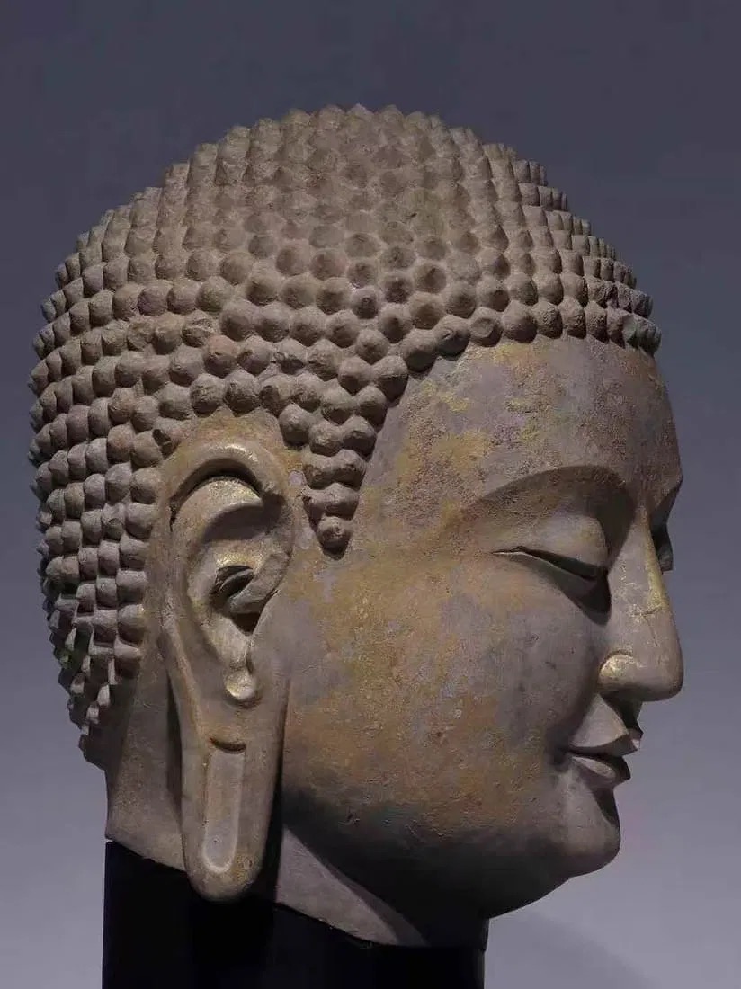 A serene stone bust with a golden forehead and a black pedestal.