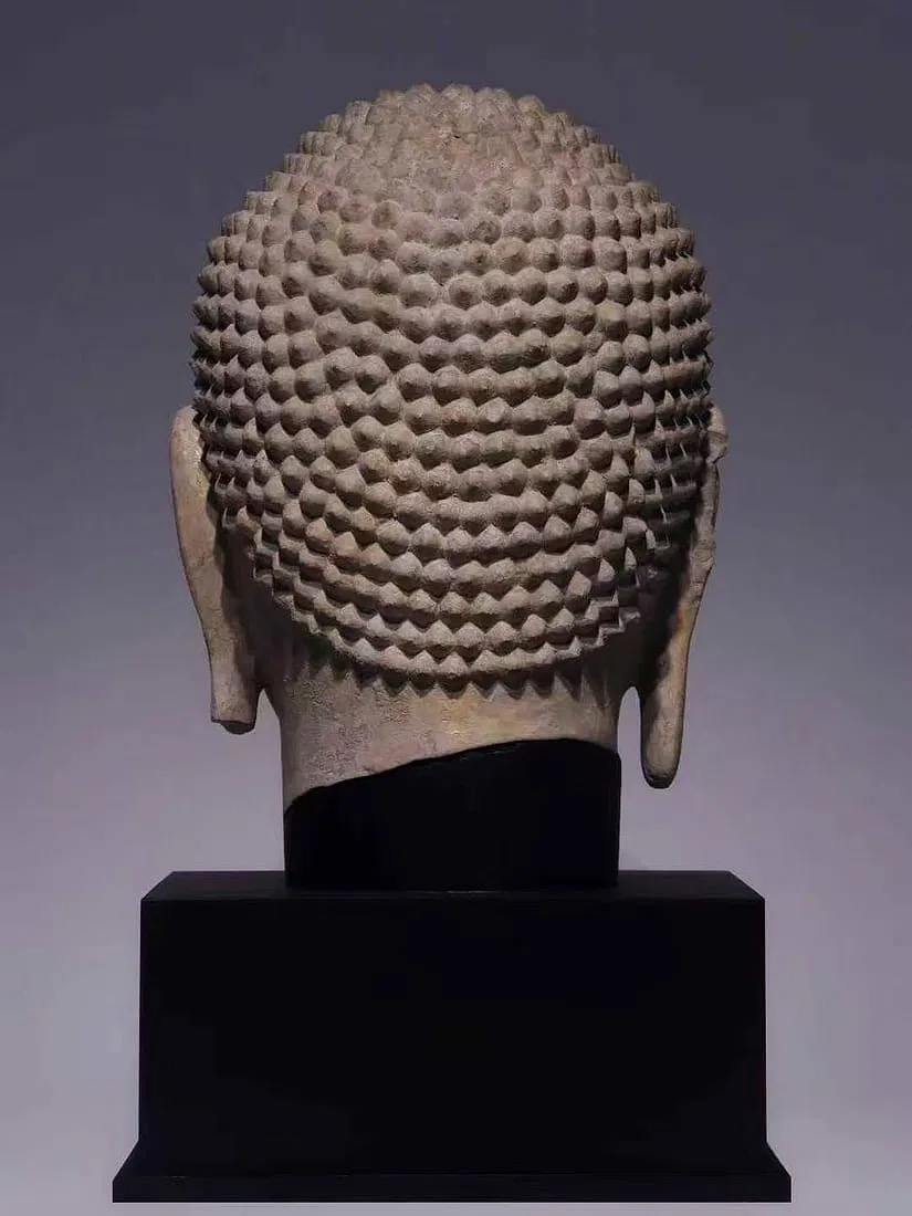 A serene stone bust with a golden forehead and a black pedestal.
