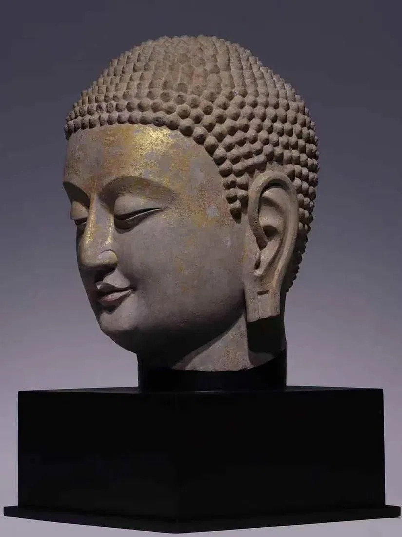 A serene stone bust with a golden forehead and a black pedestal.