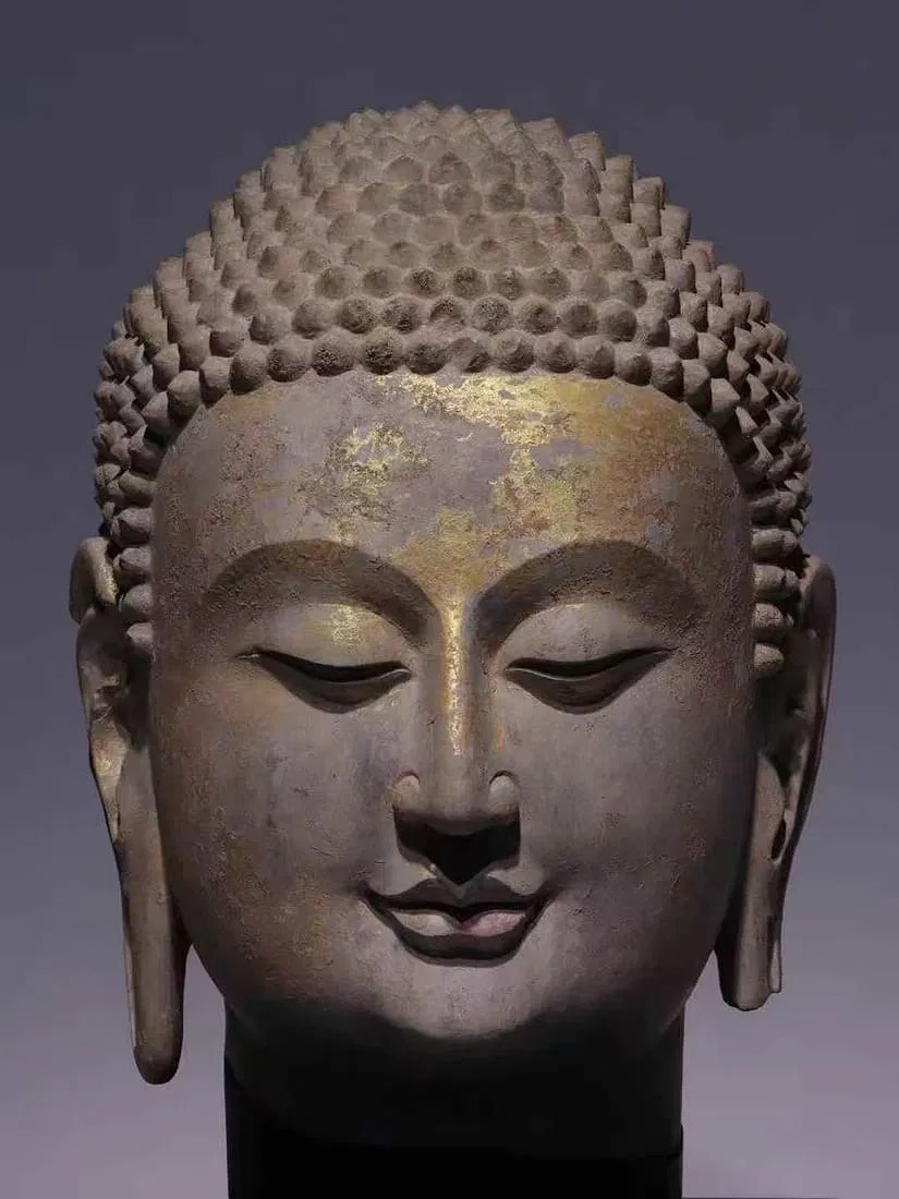 A serene stone bust with a golden forehead and a black pedestal.